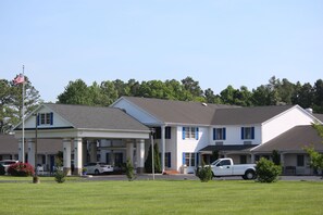 A motel with a covered front porch, a flagpole with an American flag, and a white pickup truck parked in front.