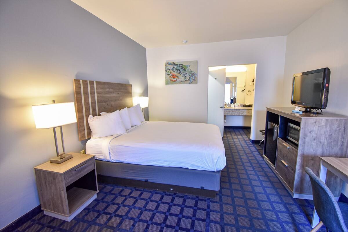A hotel room with a bed, bedside lamp, TV, and a small desk with a chair.
