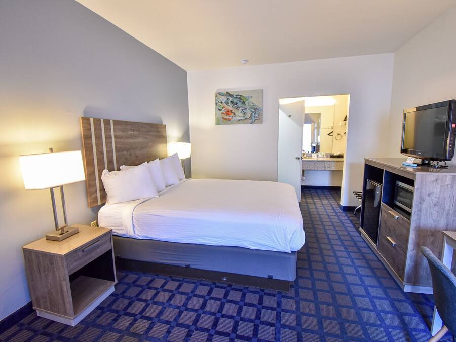 Quarto de hotel com cama, abajur, televisão e uma pequena mesa com cadeira.