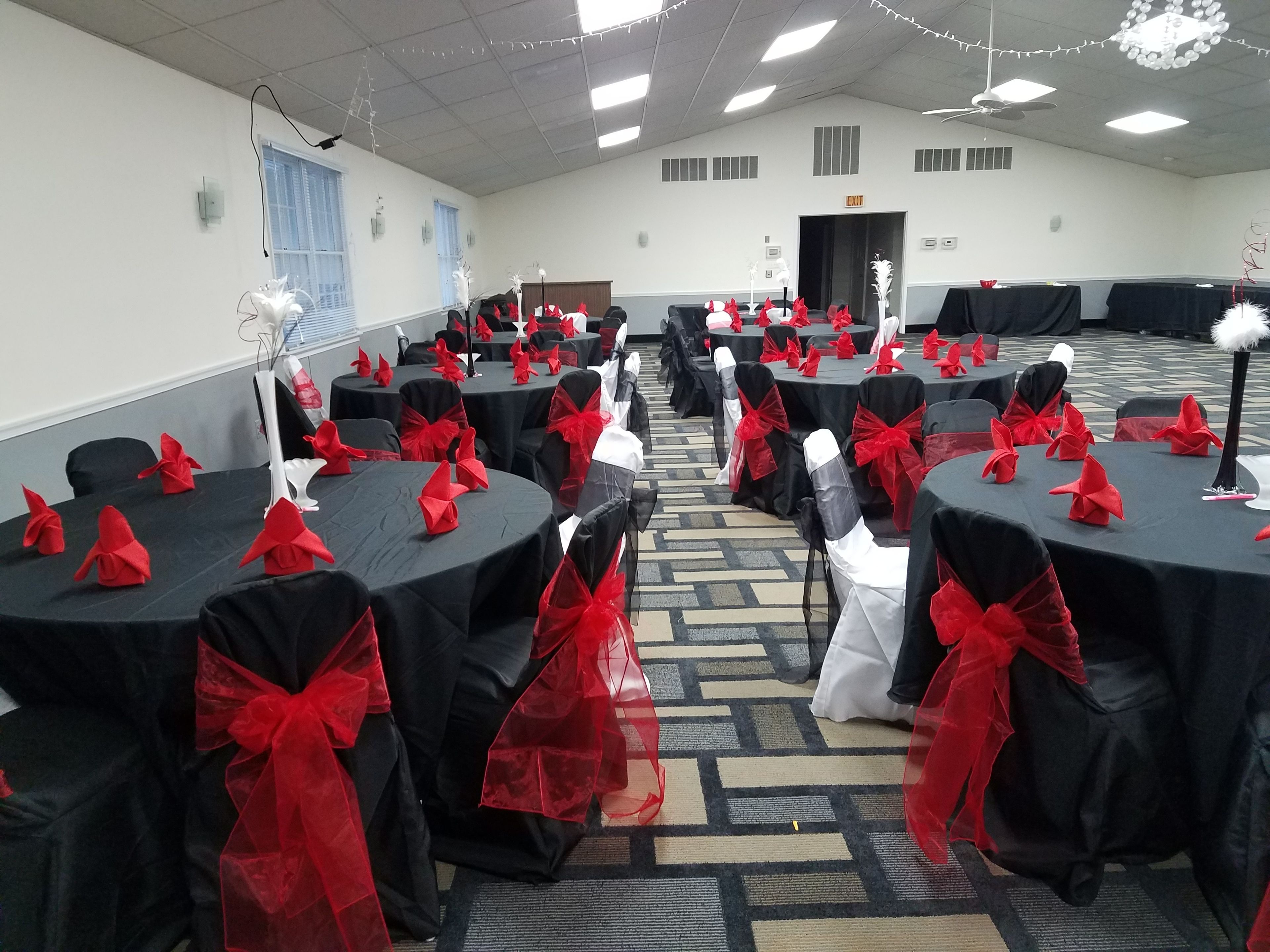 Un salón de conferencias con mesas redondas, cada una con mantel negro y fajas rojas.