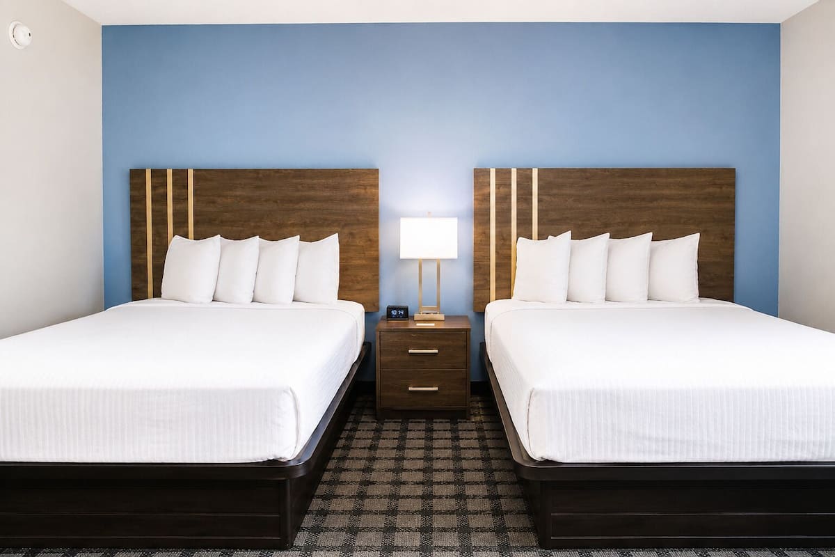 A hotel room with two beds, a nightstand with a lamp, and a checkered floor.