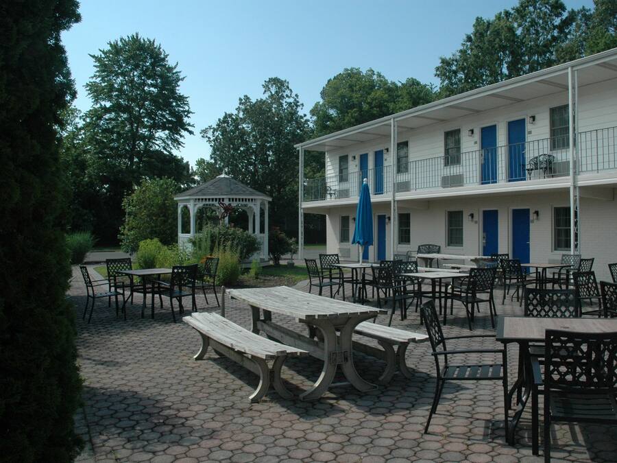 An outdoor patio area with picnic tables and chairs, a gazebo, and a two-story building with blue doors and windows.