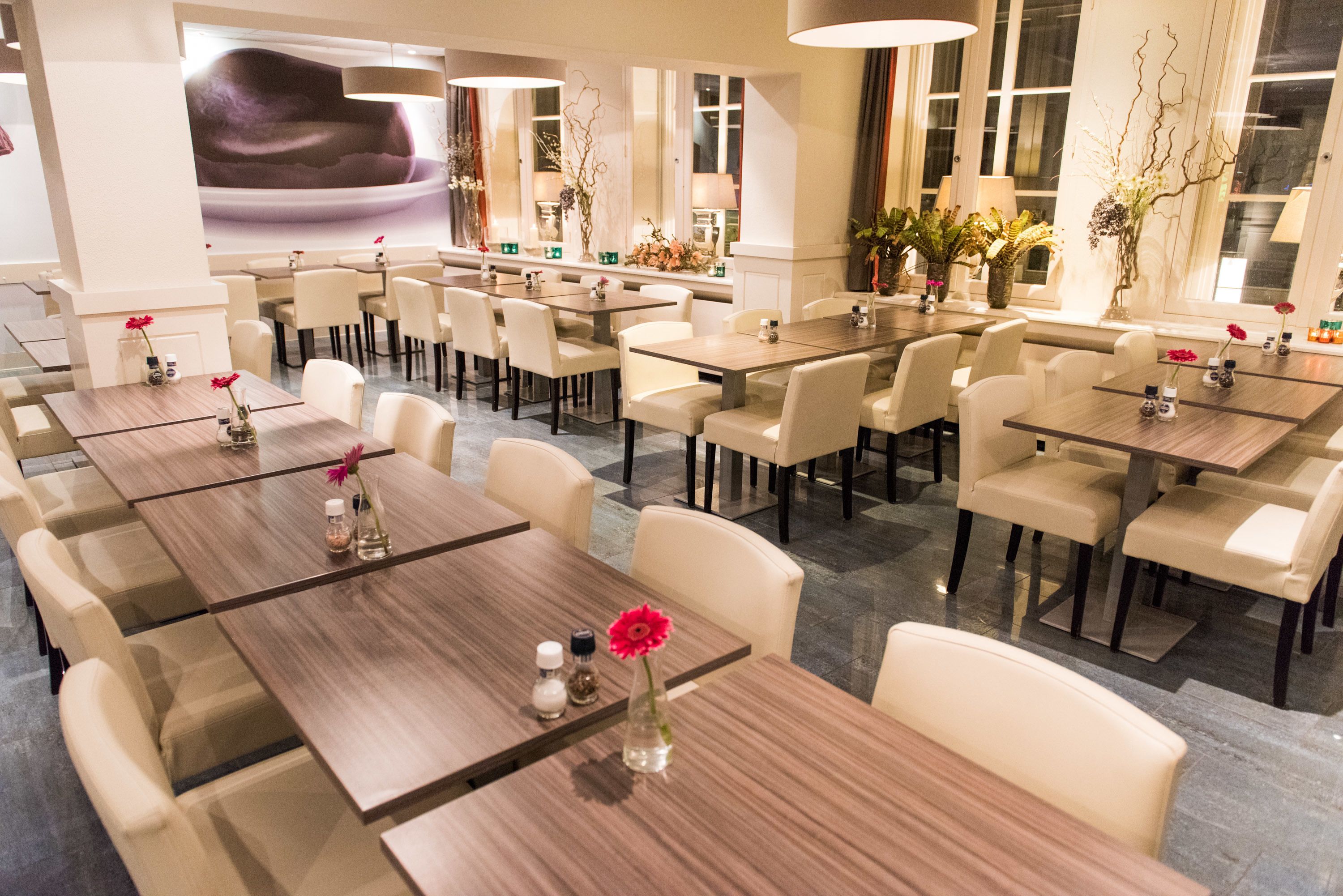 Een restaurantgedeelte van een hotel met meerdere tafels en stoelen, in een ruim opgezette indeling.