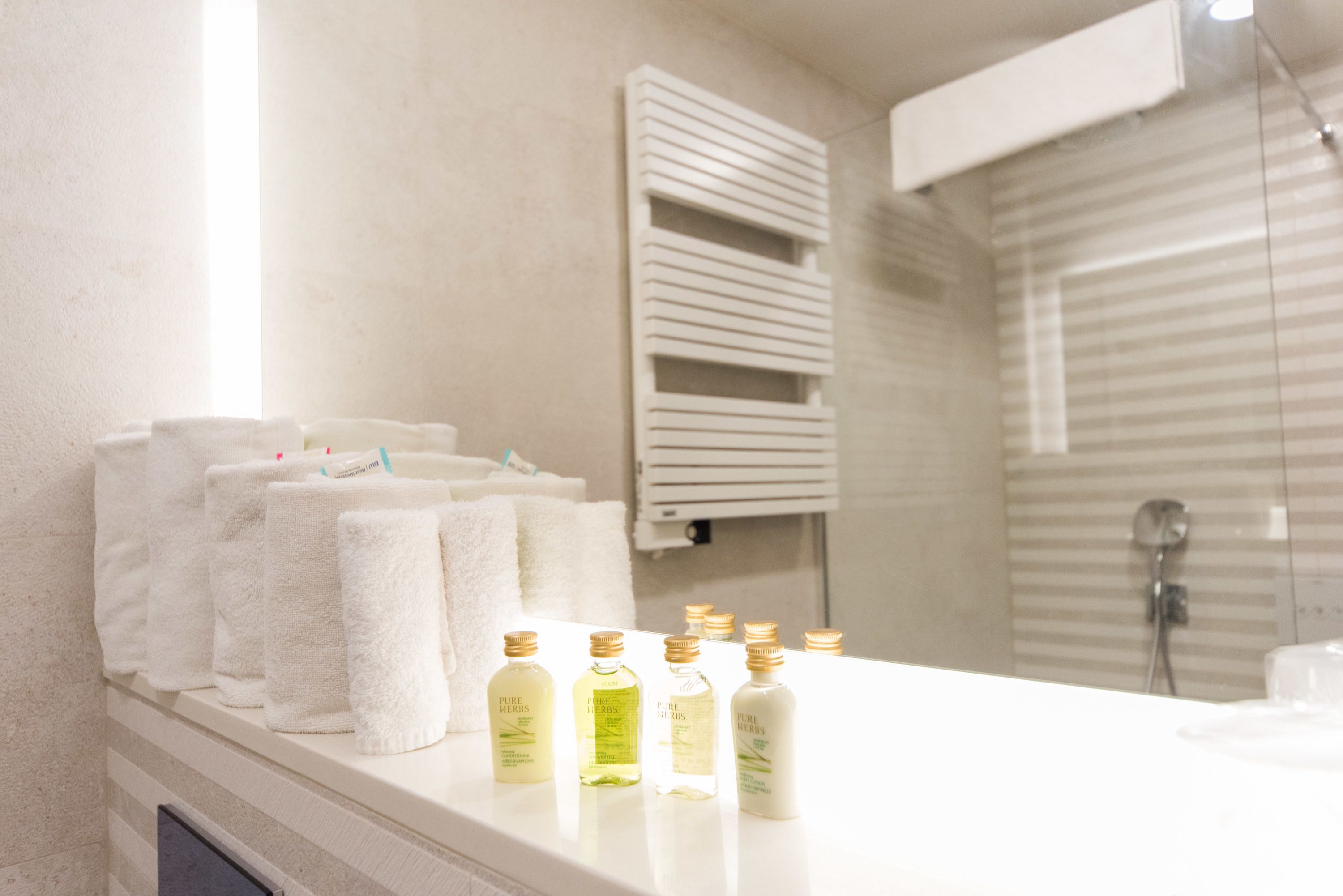A bathroom with a white countertop, several towels, and bottles of toiletries.