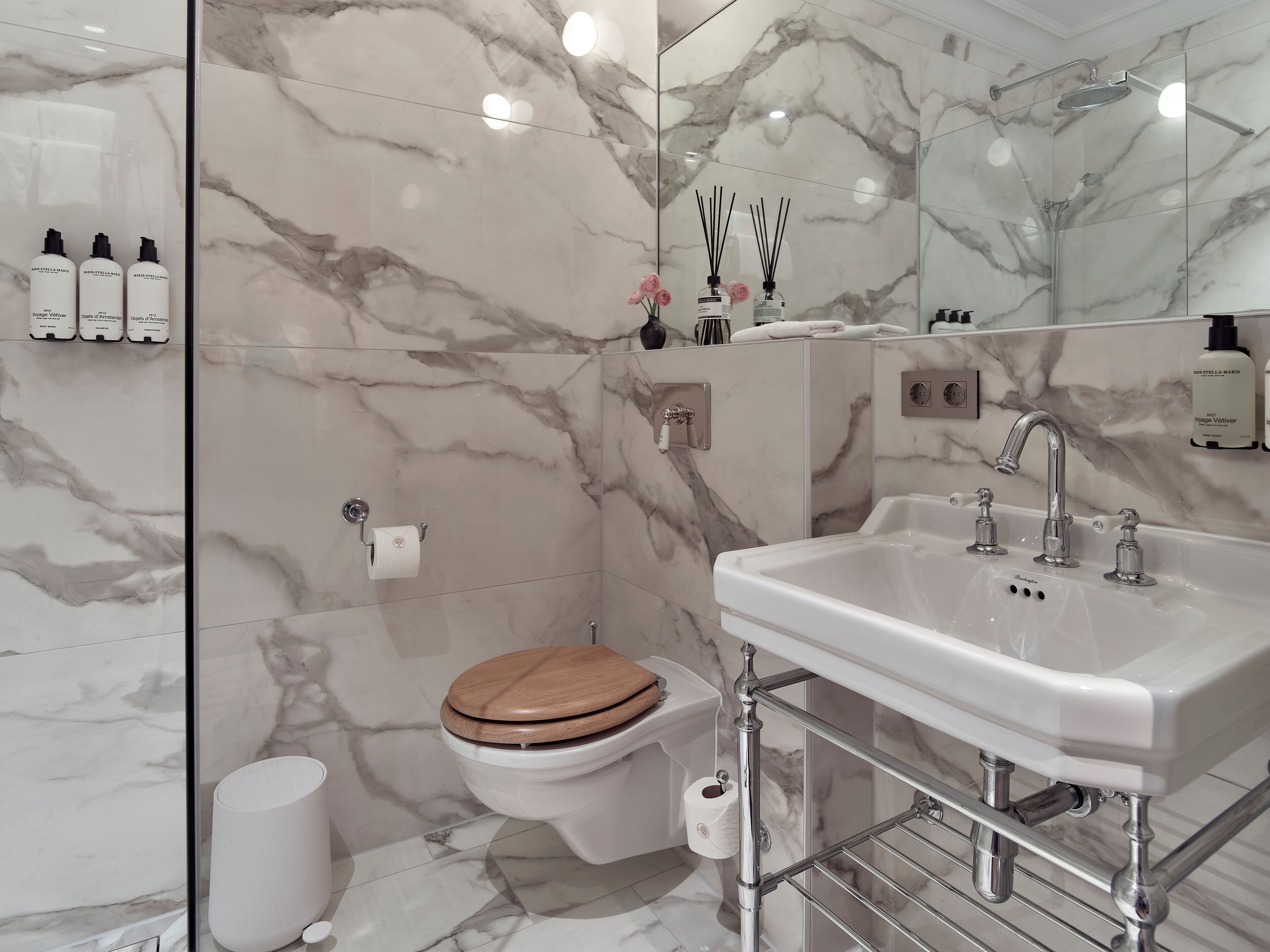 A modern bathroom with a marble backsplash, a white sink, and a wooden toilet.