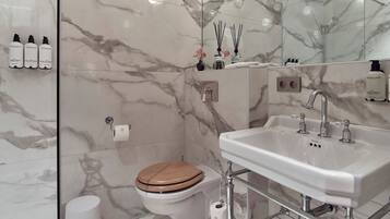 A modern bathroom with a marble backsplash, a white sink, and a wooden toilet.