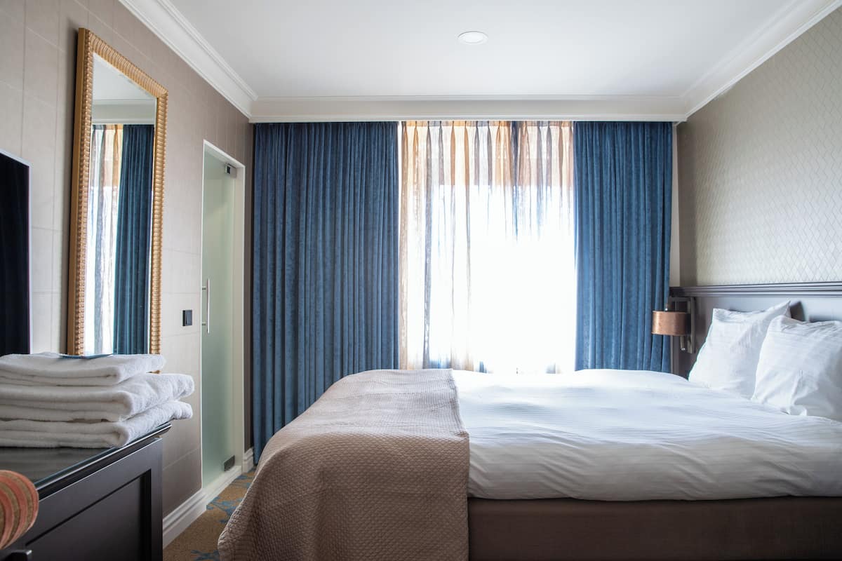 Une chambre d’hôtel avec un lit, un grand miroir, un bureau avec une chaise et une fenêtre avec des rideaux.