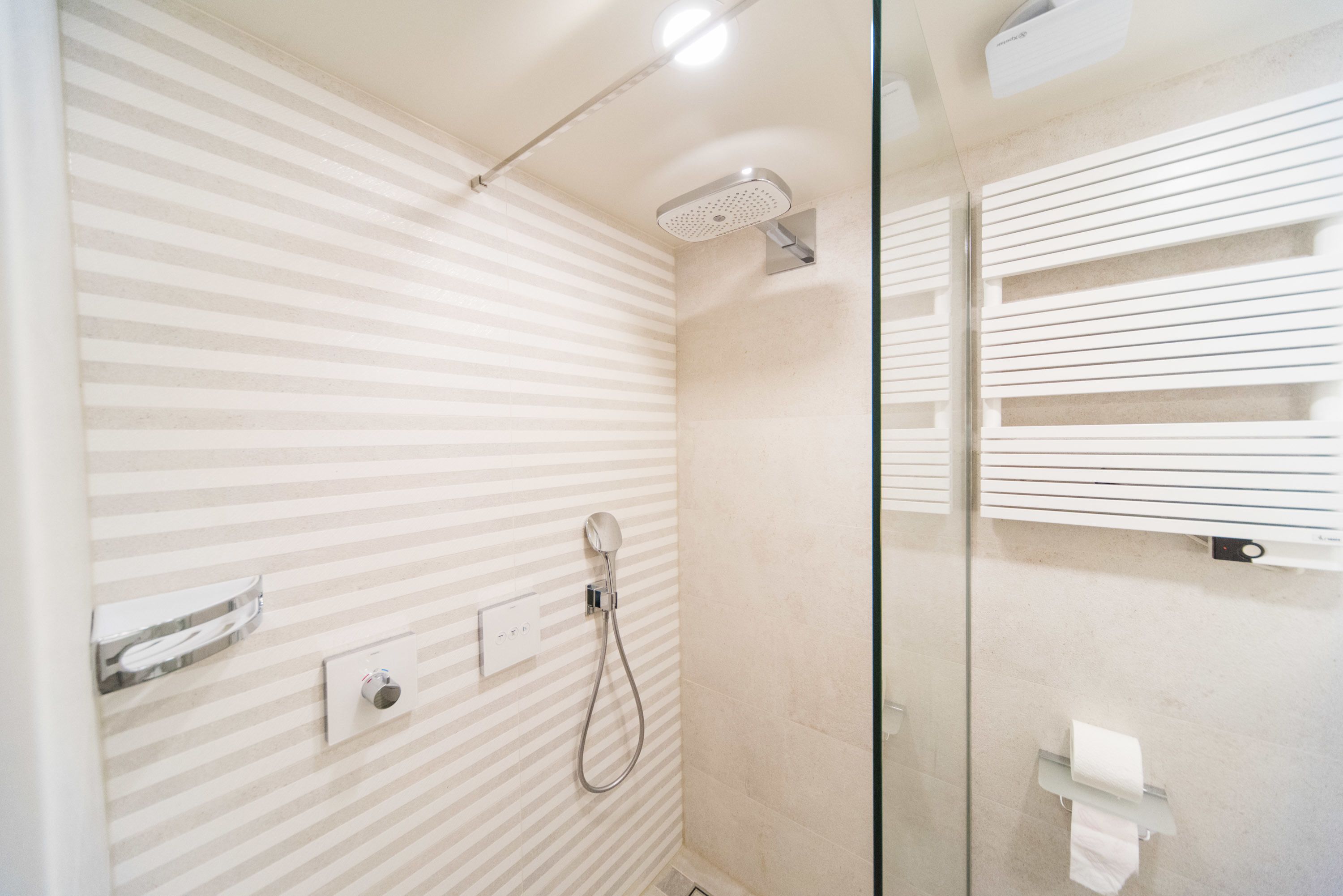 A modern bathroom with striped walls, a glass shower enclosure, and a towel rack.