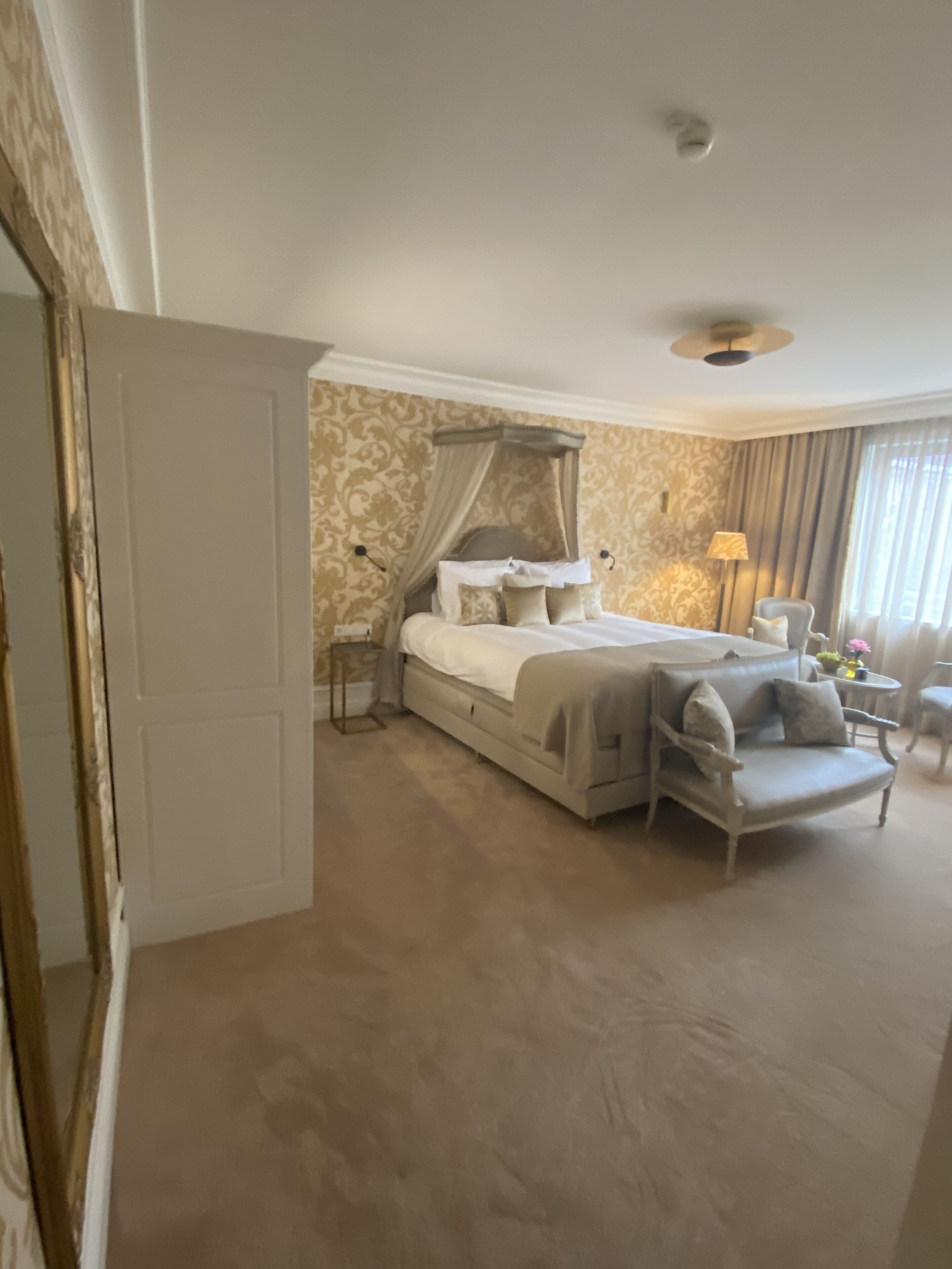 A bedroom with a canopy bed, a sitting area with a sofa, and a lamp.