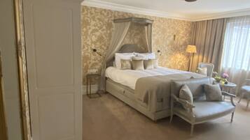 A bedroom with a canopy bed, a sitting area with a sofa, and a lamp.