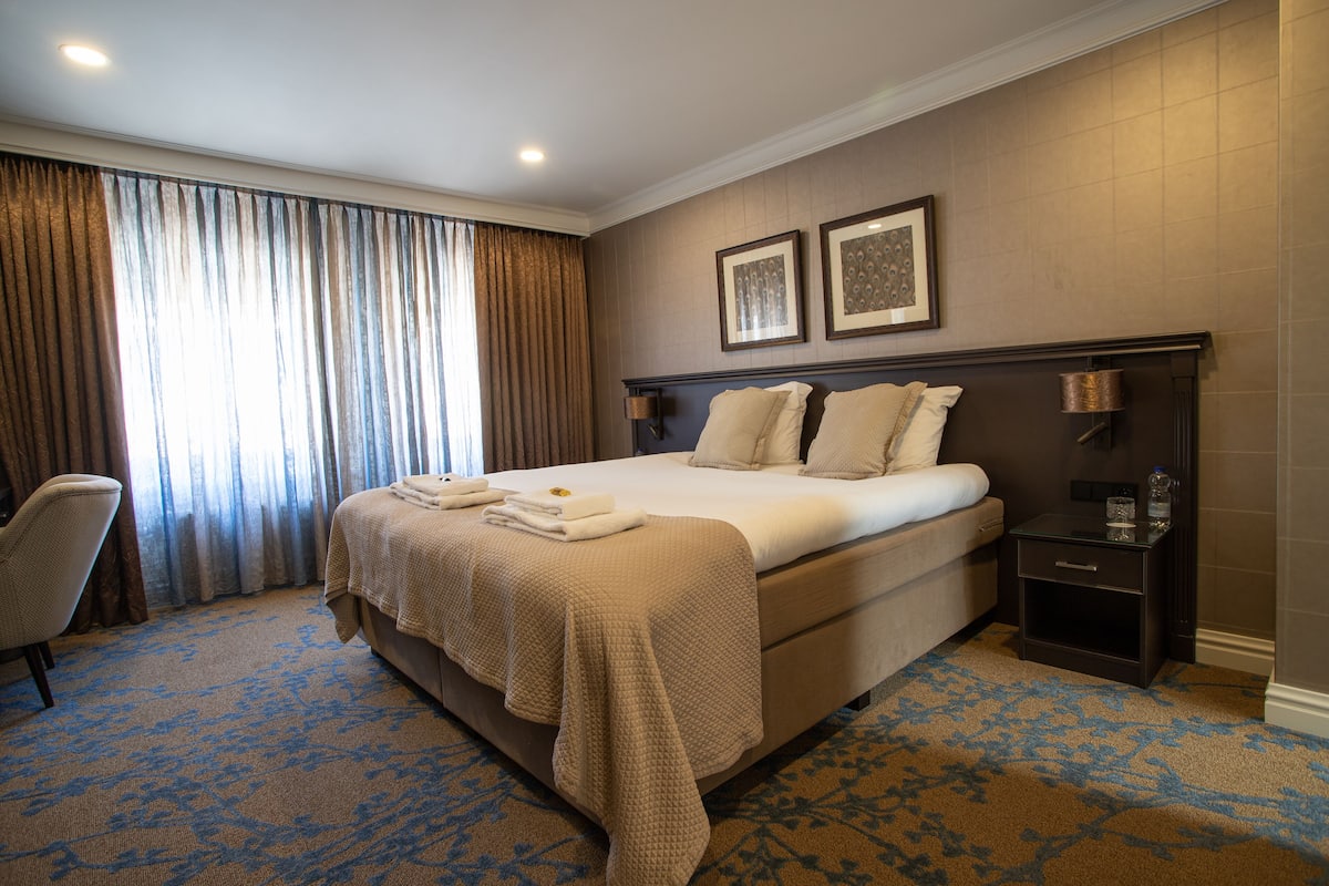 Une chambre d’hôtel avec un grand lit, une chaise, une table de chevet et une fenêtre avec des rideaux.