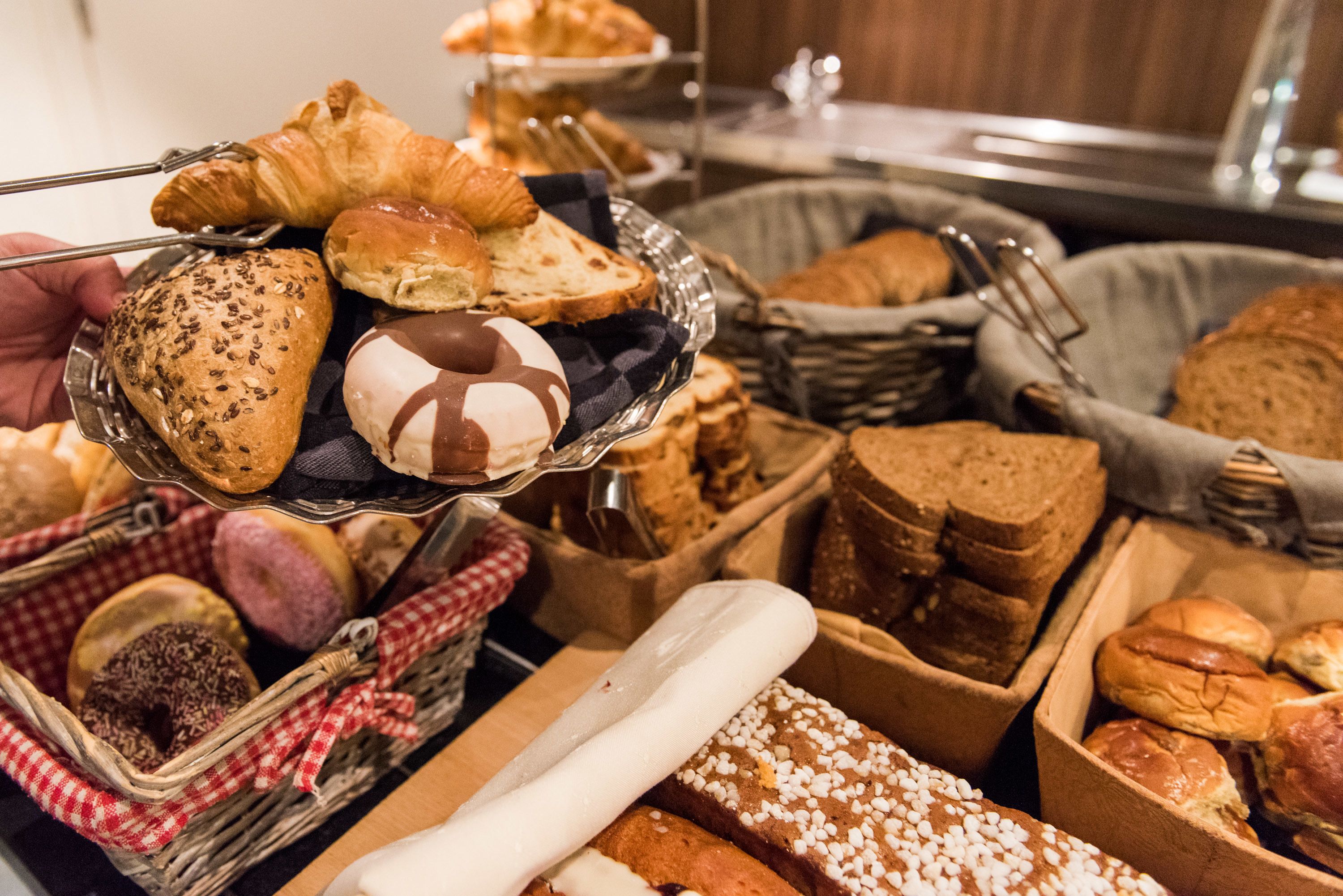 A variety of baked goods including bread, pastries, and donuts displayed in baskets and on a serving tray.
