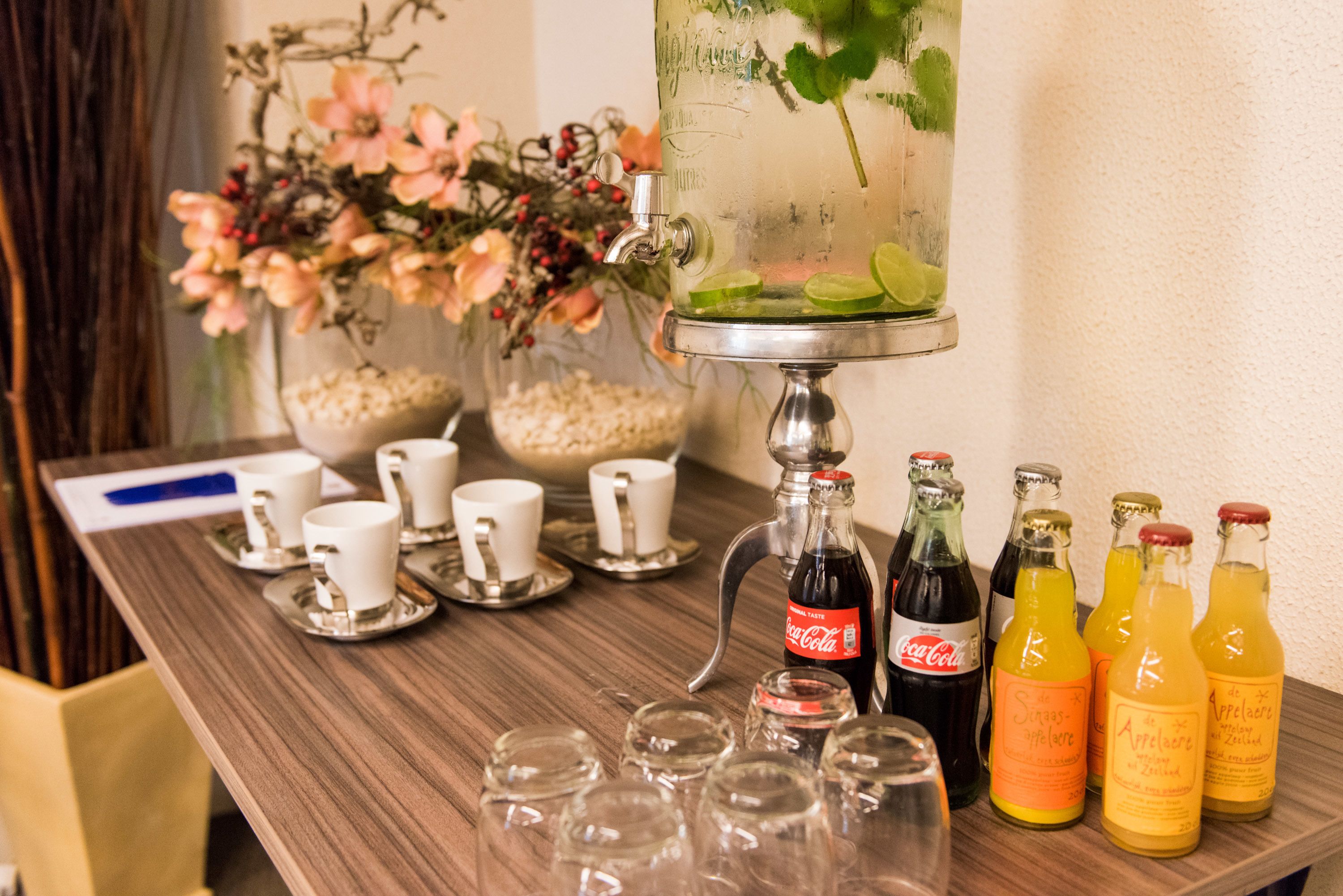 Uma área de bar com um grande dispensador de água, várias garrafas de bebidas e um arranjo floral.