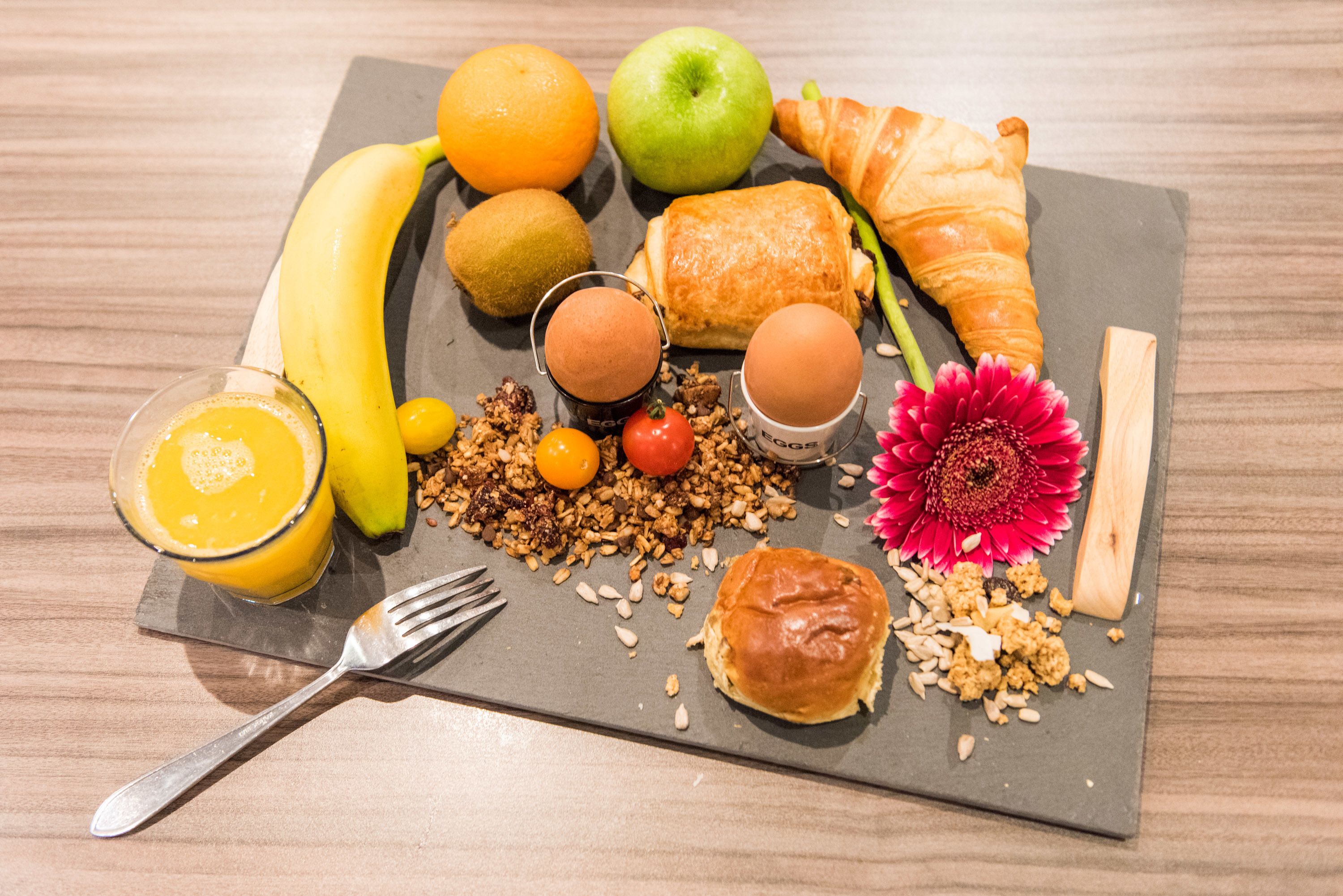 A breakfast spread on a slate board including fruits, pastries, and a drink.