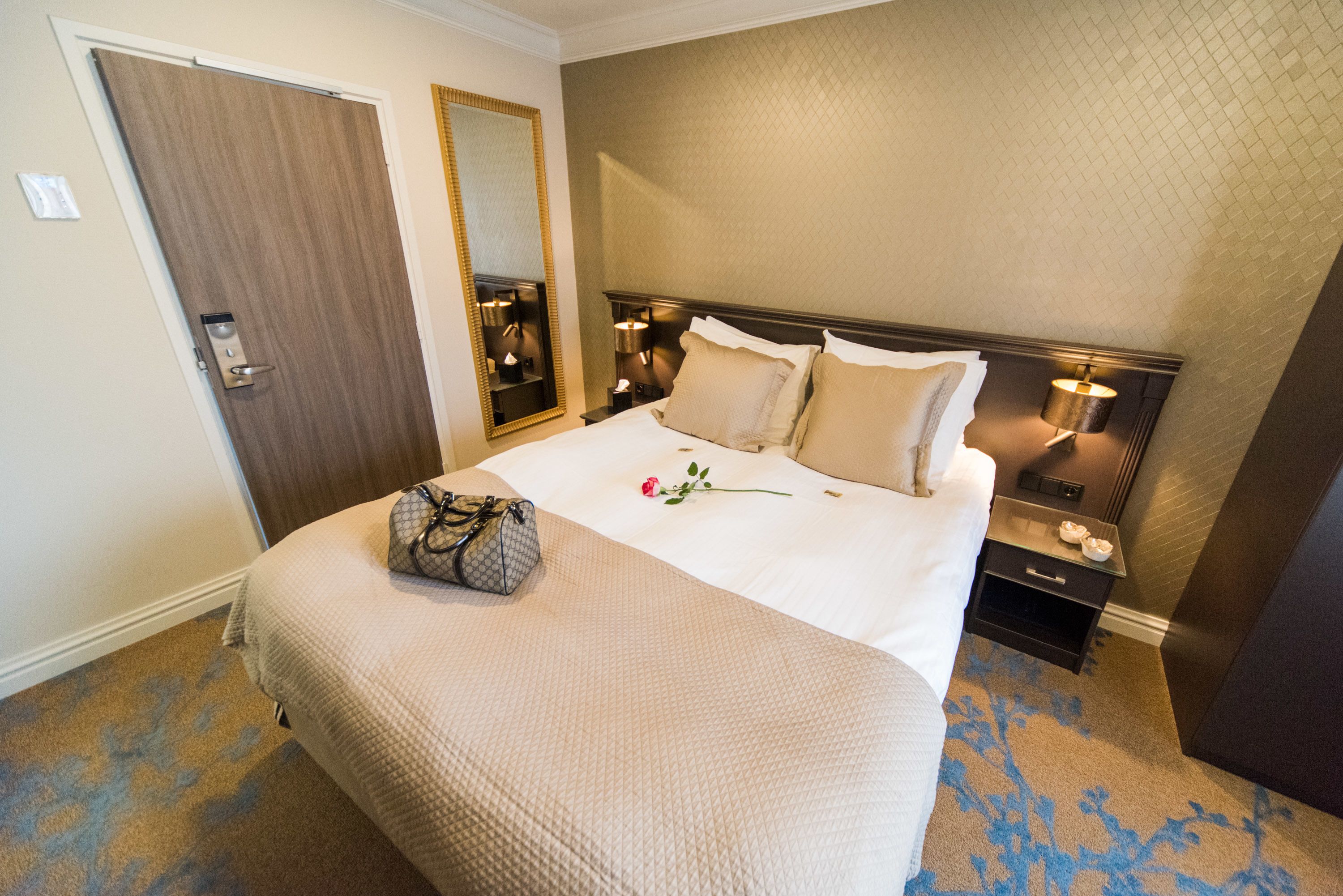 Een hotelkamer met een groot bed, een nachtkastje, een spiegel en een deur.