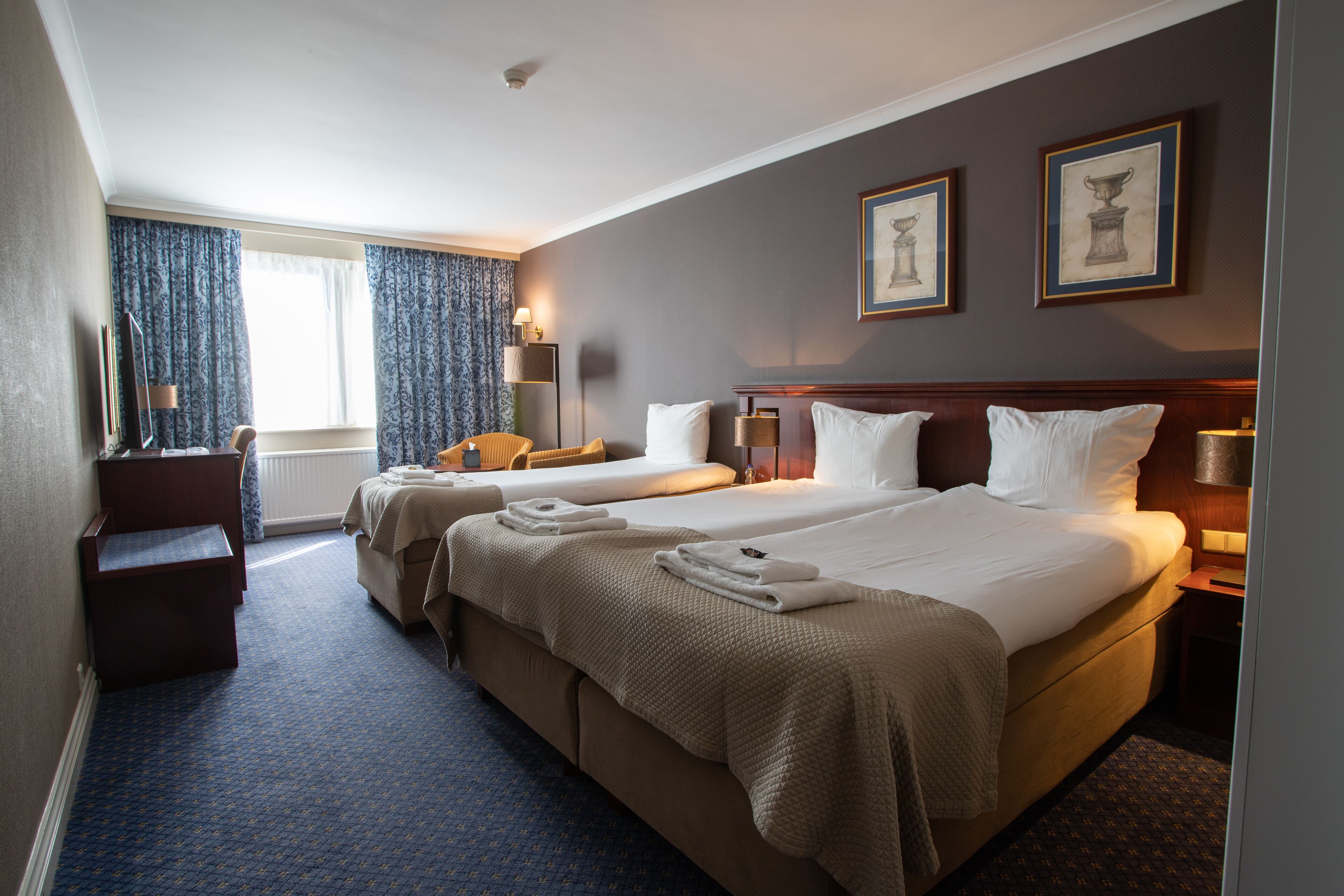 A hotel room with two beds, a desk, a chair, and a window with curtains.