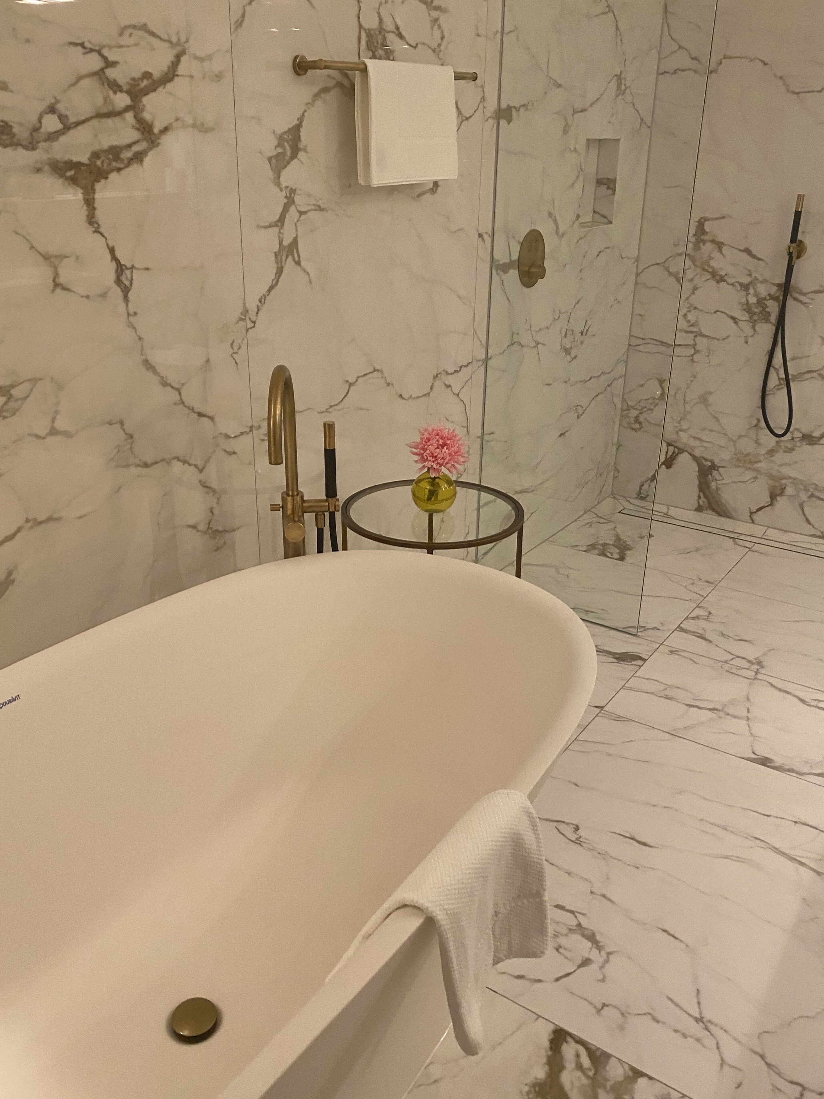 Un baño moderno con una bañera independiente, una mesita redonda pequeña con un florero y un perchero en la pared.