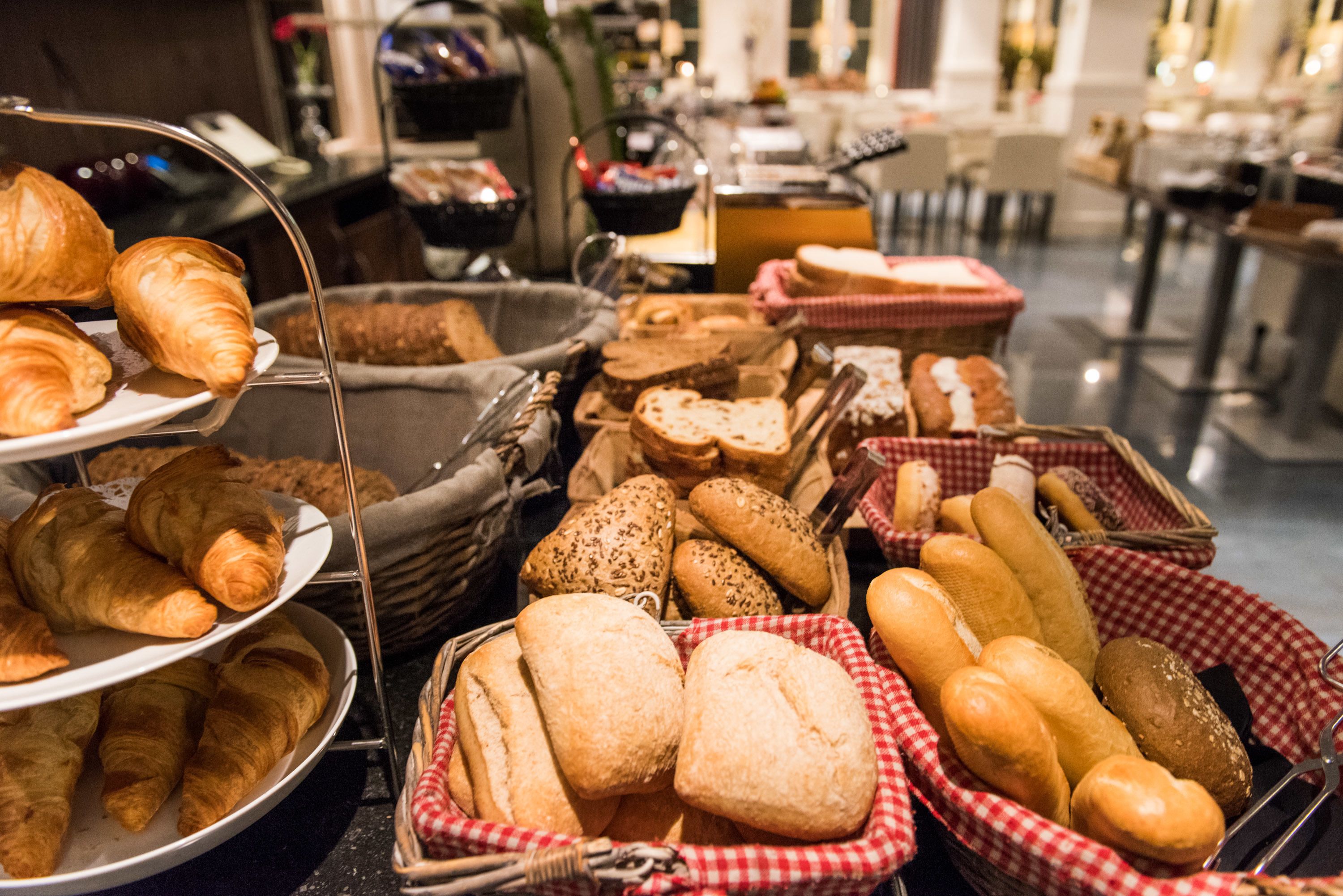 A variety of baked goods including croissants, baguettes, and other breads displayed in baskets and on plates.