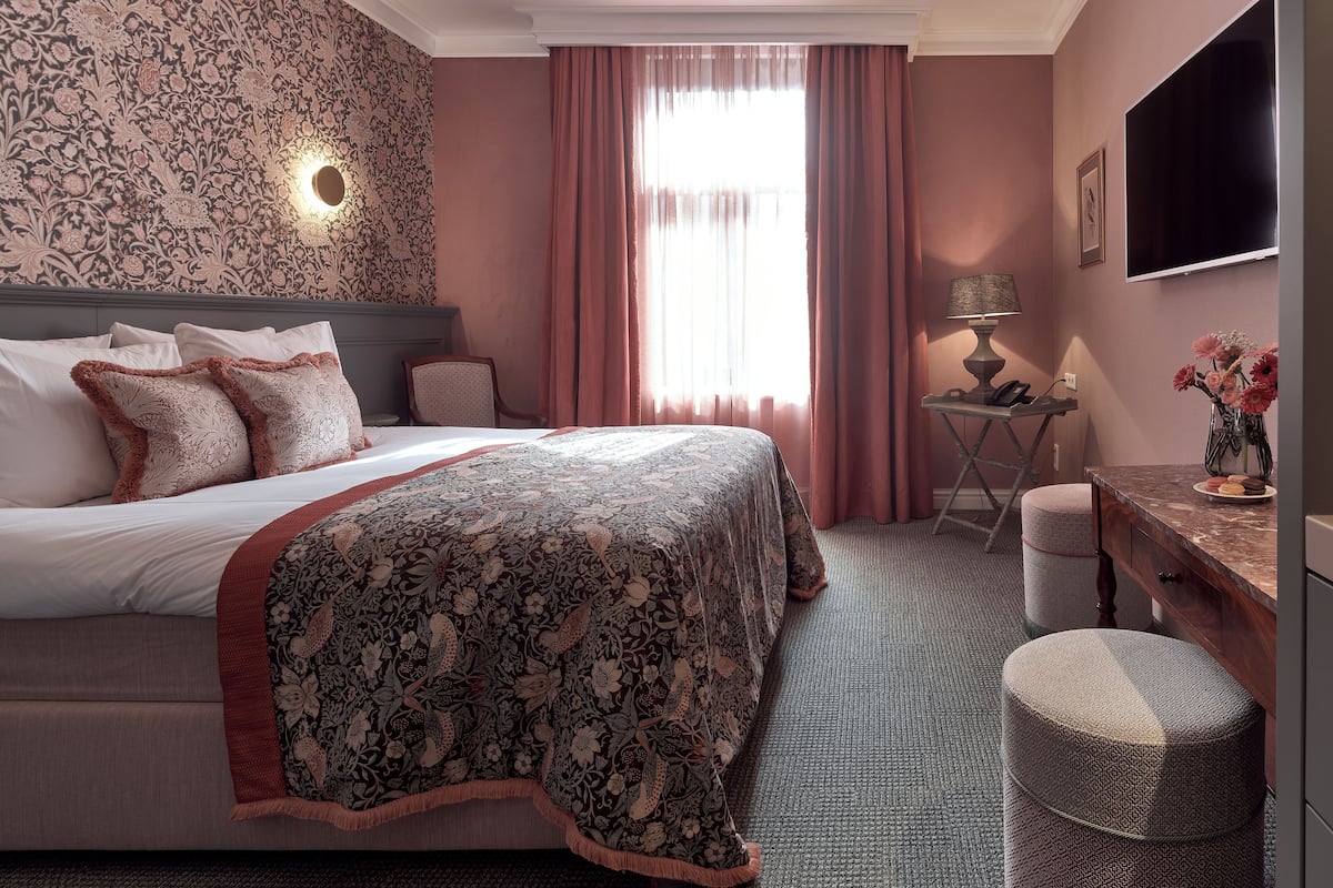 Une chambre d’hôtel avec un grand lit, un bureau, une chaise, une télévision et une fenêtre avec des rideaux.