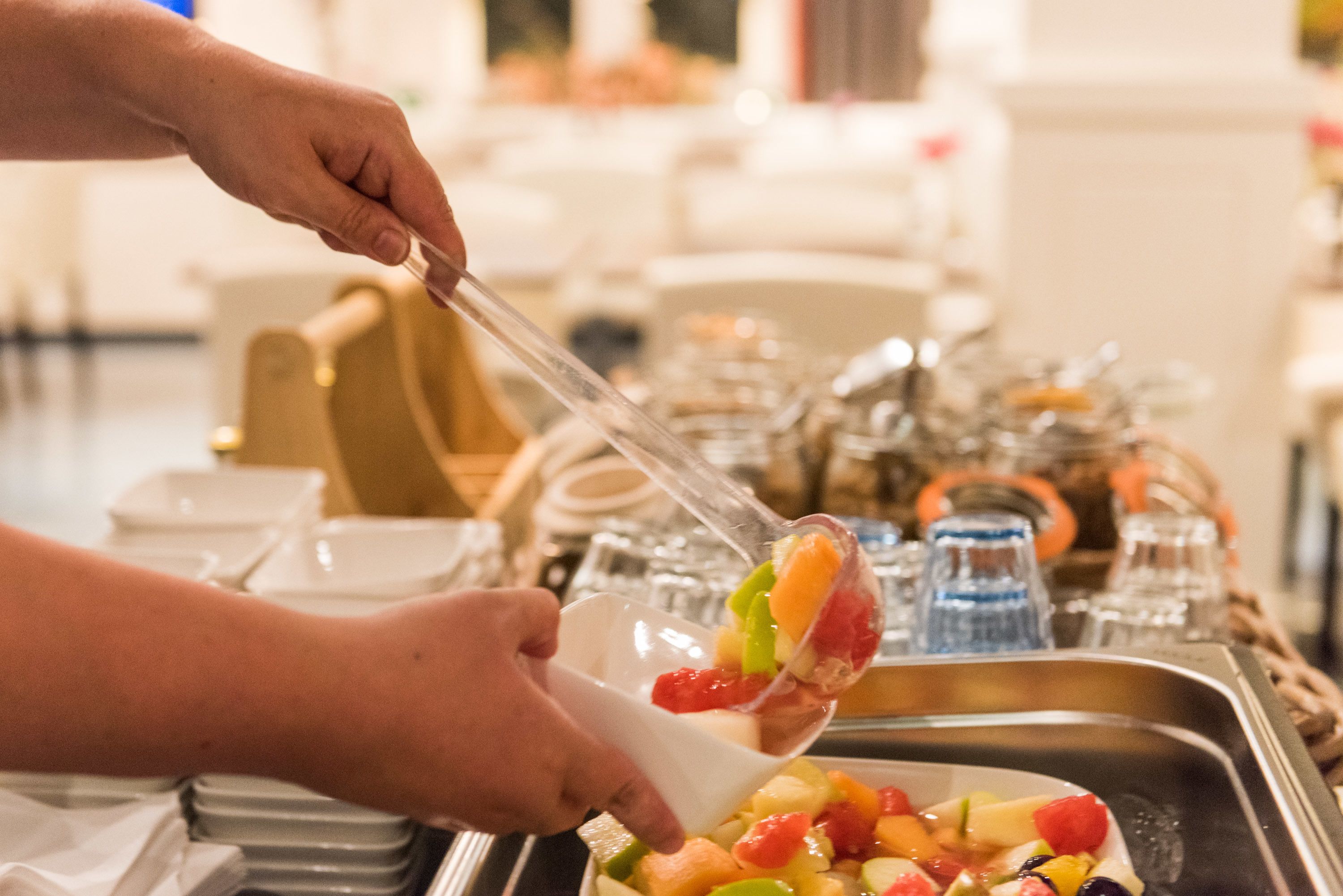 A person serving fruit from a buffet.