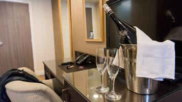 A hotel room with a minibar, a mirror, a desk with a phone, and two empty wine glasses.