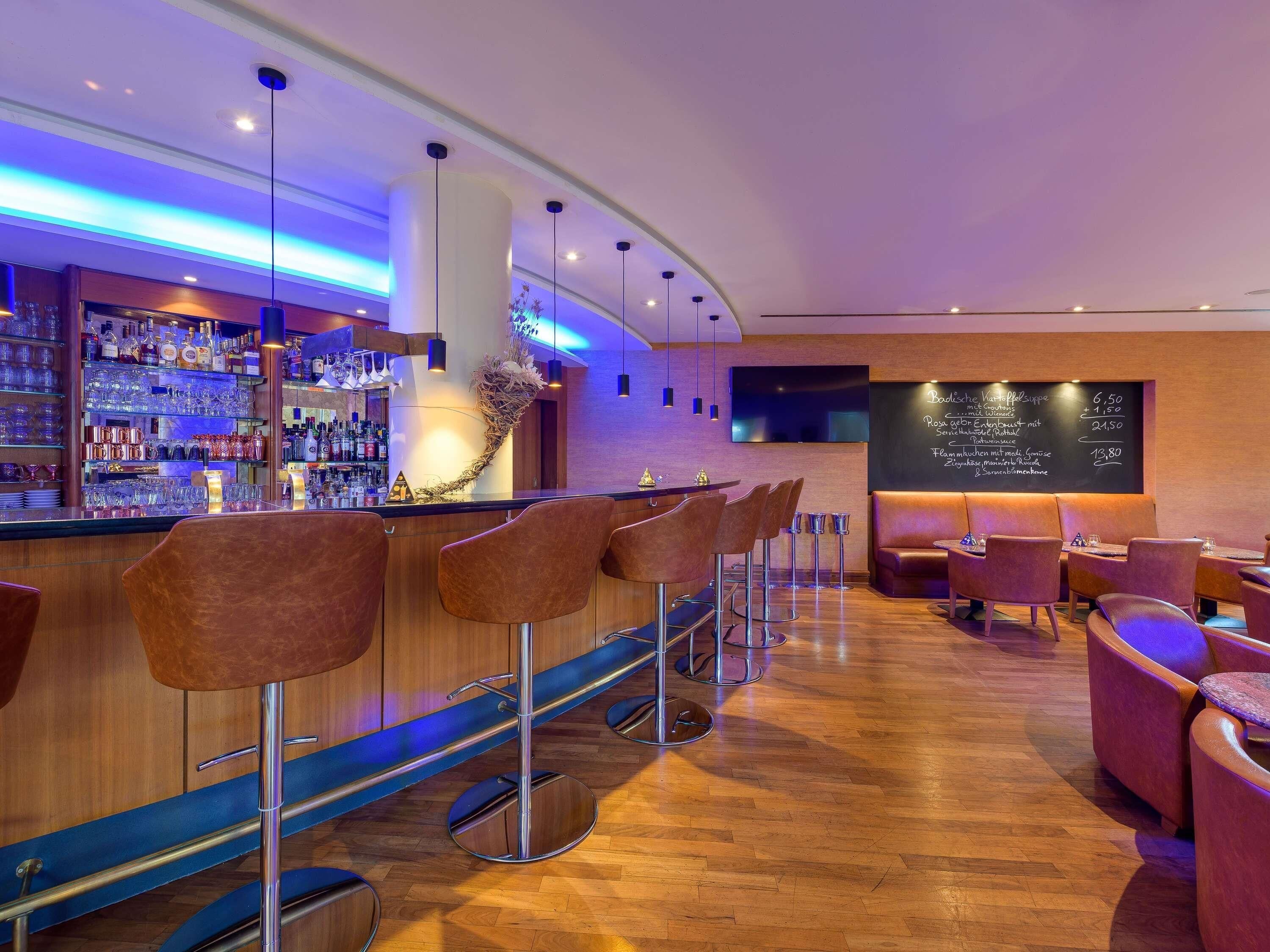 A bar area with a wooden bar counter, multiple stools, and a menu board.