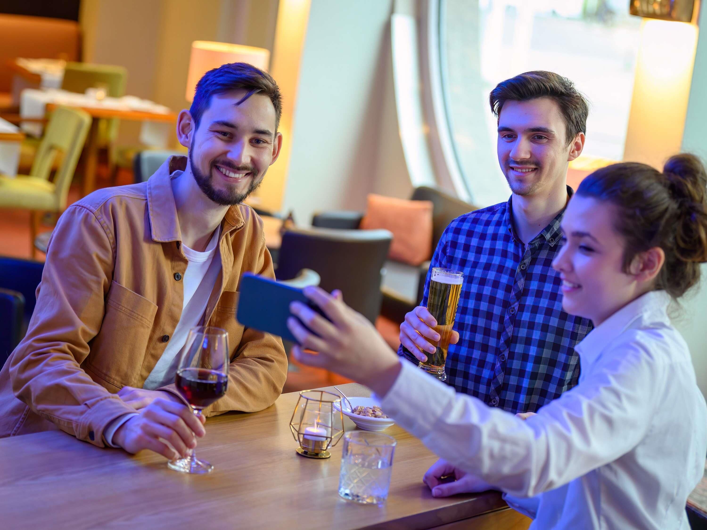Un groupe de personnes est assis à une table, devant un téléphone intelligent, un verre de bière et un verre de vin rouge.