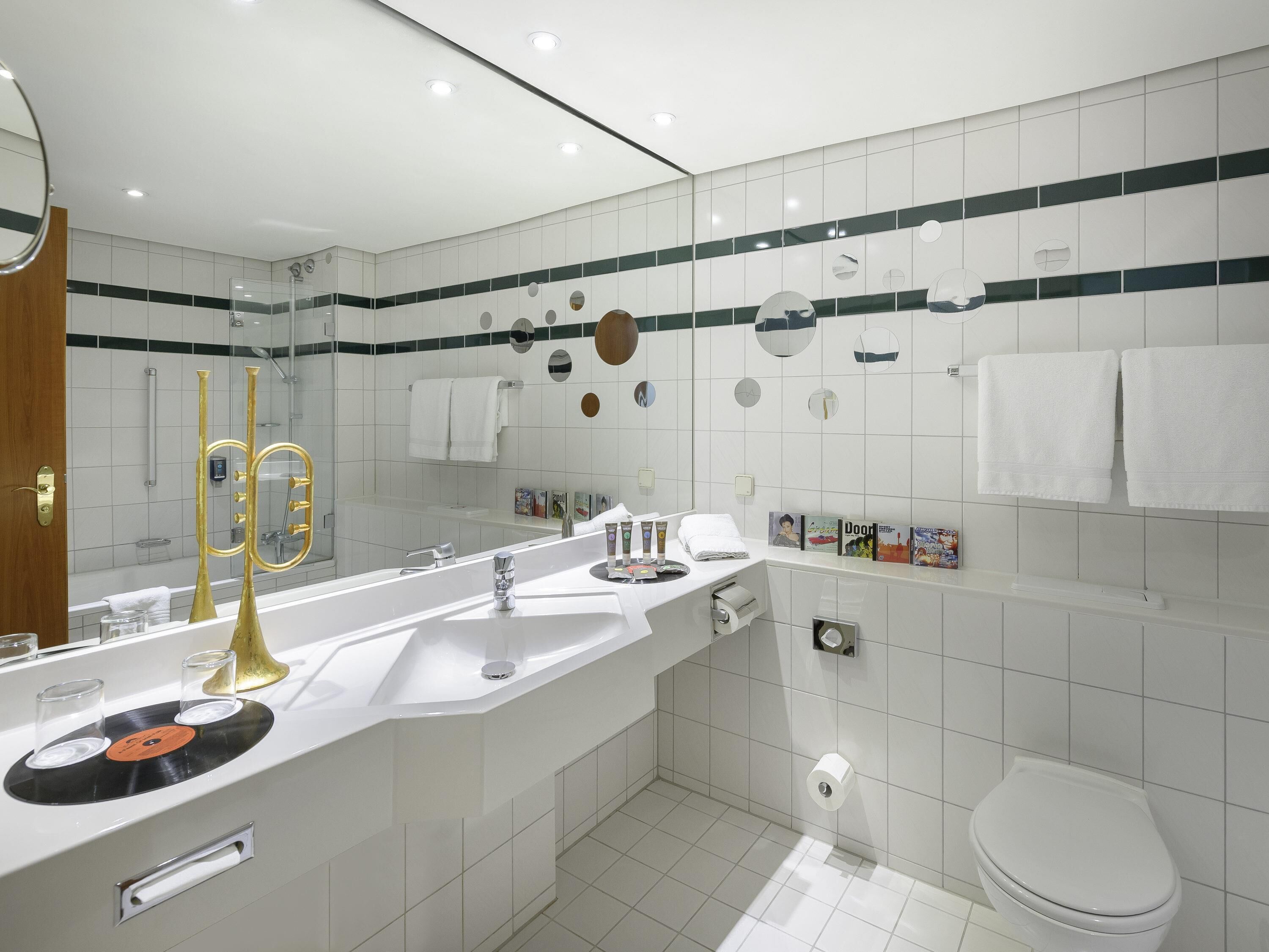 Un baño moderno con un espejo grande, azulejos blancos, una bañera y un inodoro.