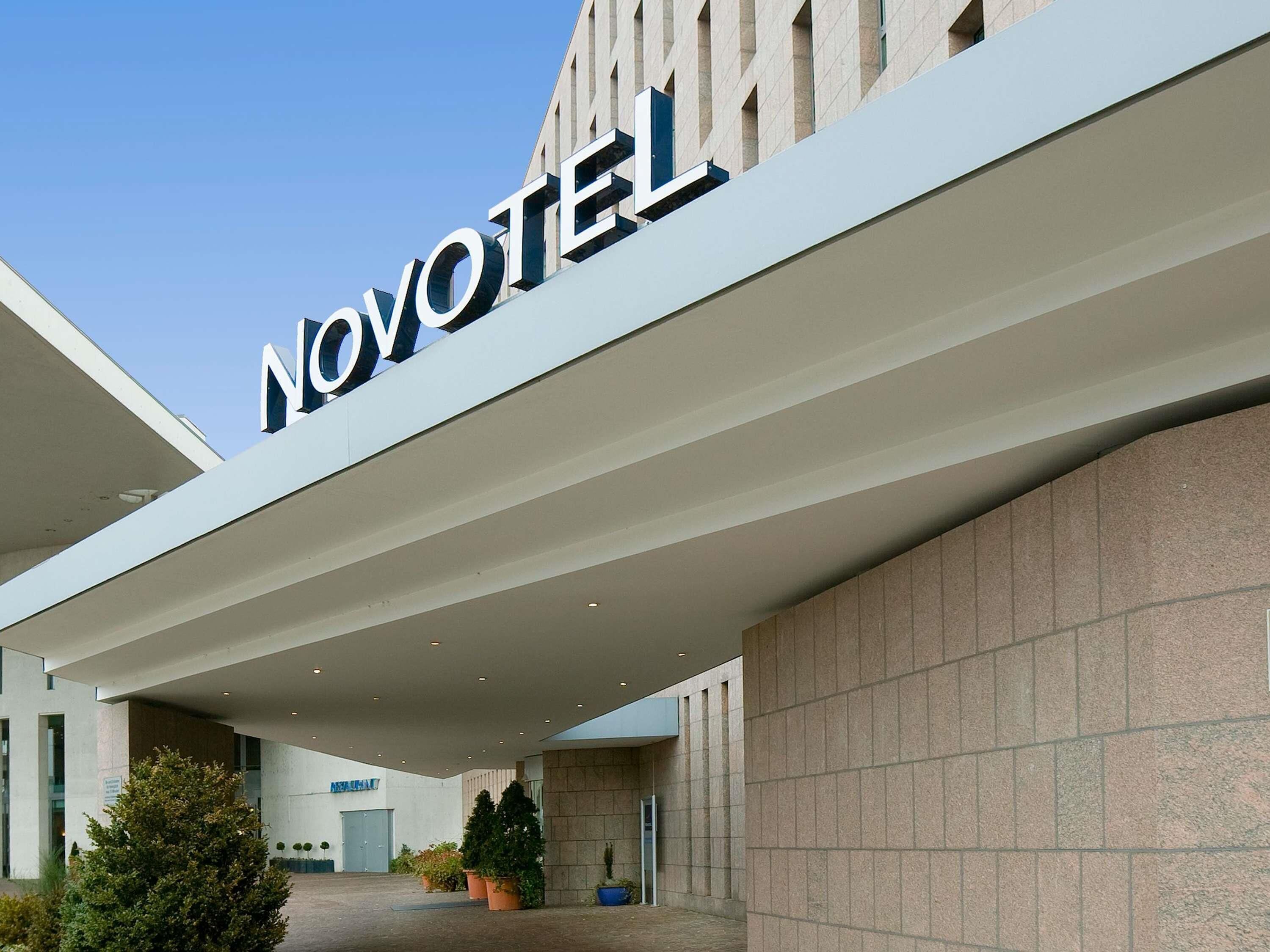 Entrada de um hotel com design moderno, exibindo uma placa chamativa com a inscrição 'NOVOTEL'.