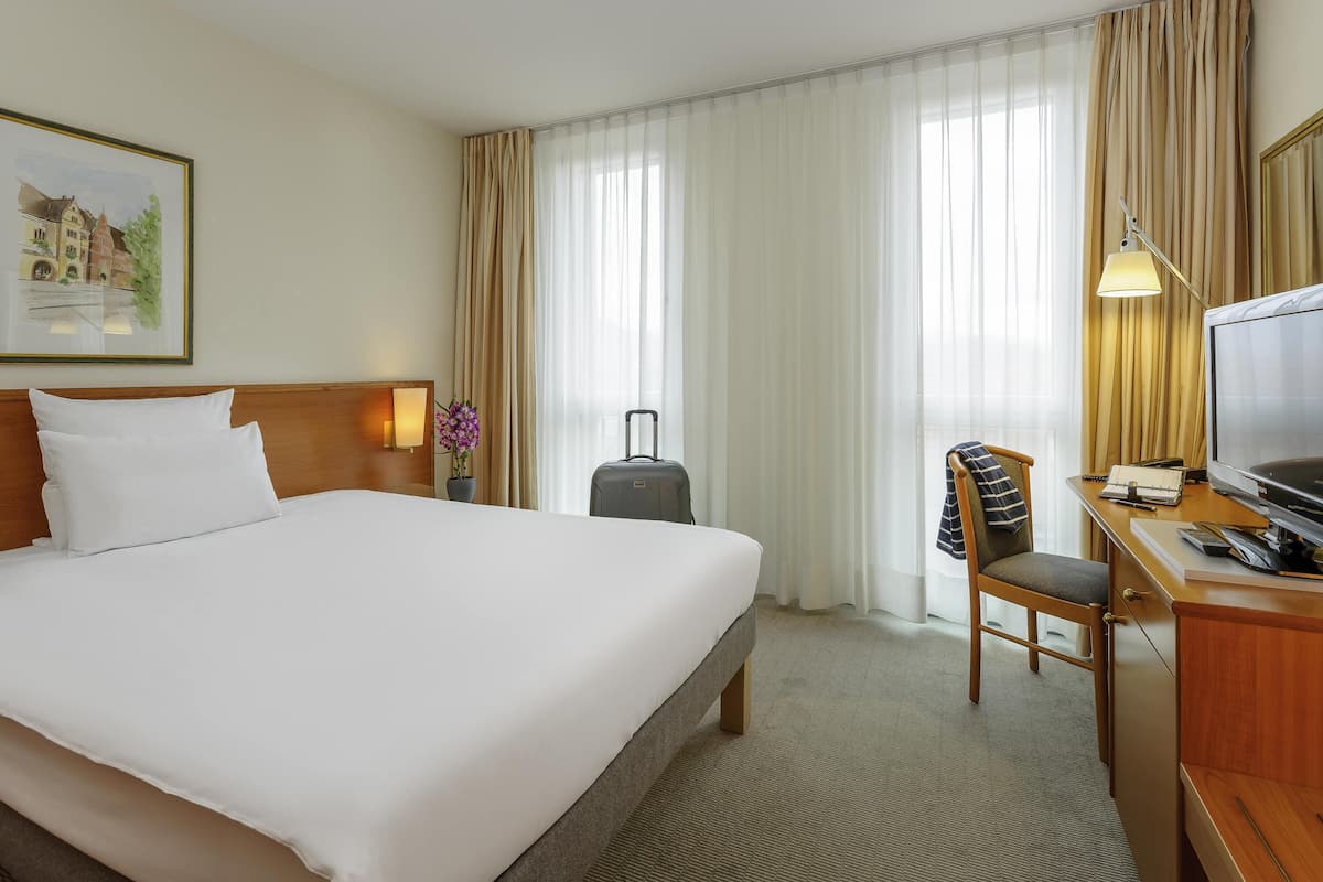 Een hotelkamer met een bed, bureau, stoel, televisie en een schilderij aan de muur.