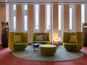 Una hall moderna con due poltrone verdi, una divano, un tavolino e un'ampia finestra con persiane verticali.