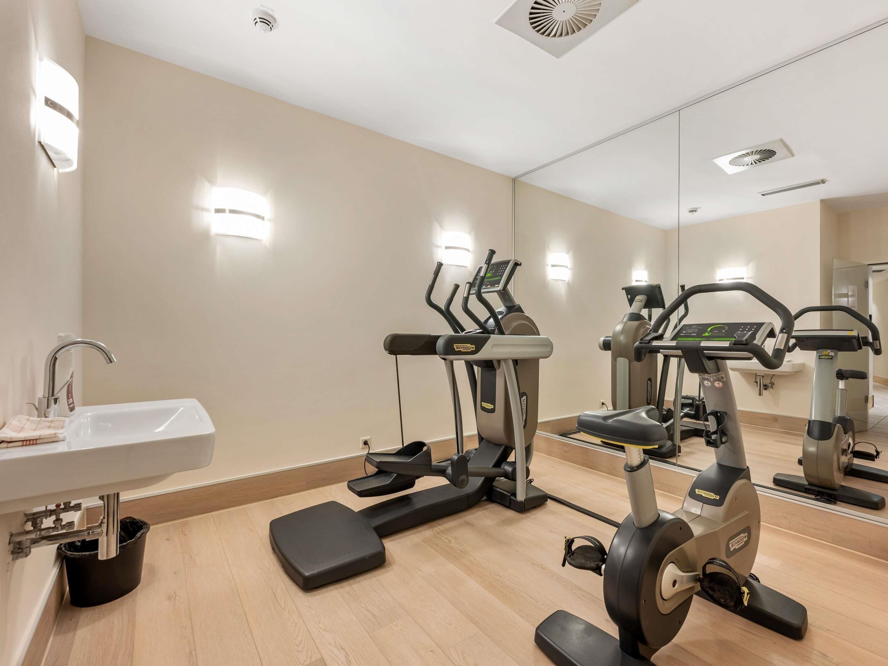 Academia moderna com pia, aparelhos de exercício e espelho refletindo o ambiente.