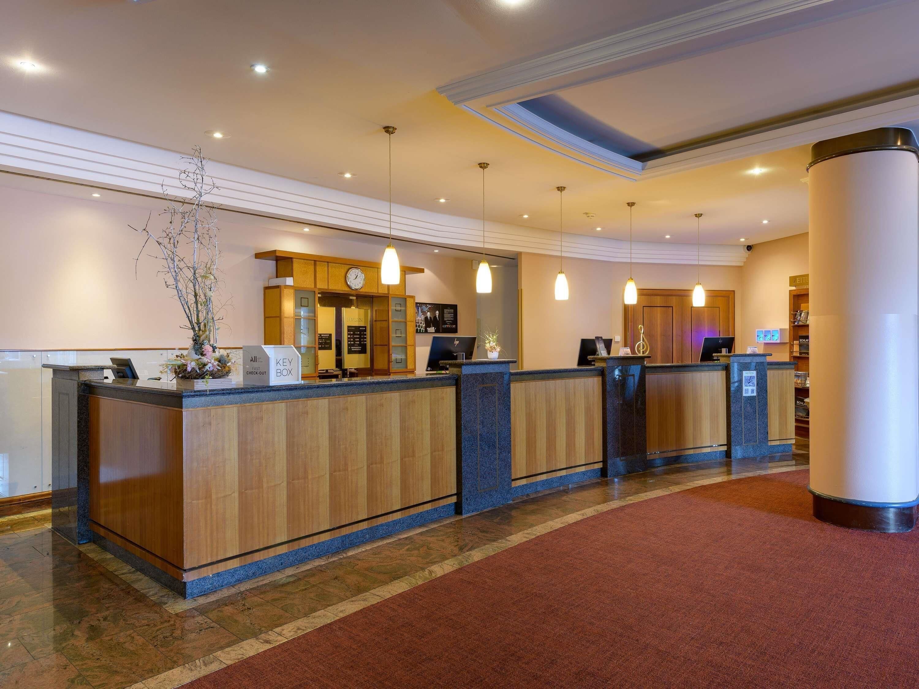 A hotel reception area with a wooden reception desk, a clock, and a key box.