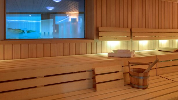 Un sauna en bois avec des bancs, un seau en bois et une grande fenêtre donnant sur l’intérieur.