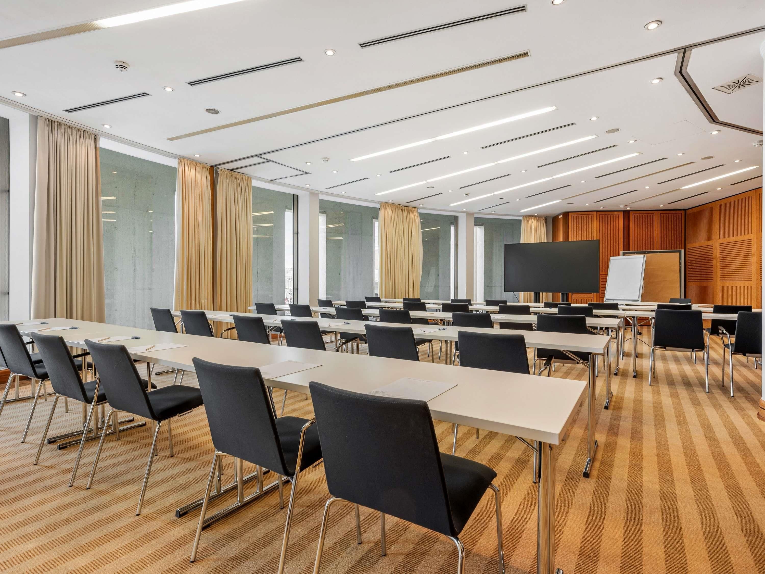 A conference room with long tables, black chairs, a large screen, and a whiteboard.