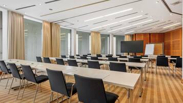 A conference room with long tables, black chairs, a large screen, and a whiteboard.