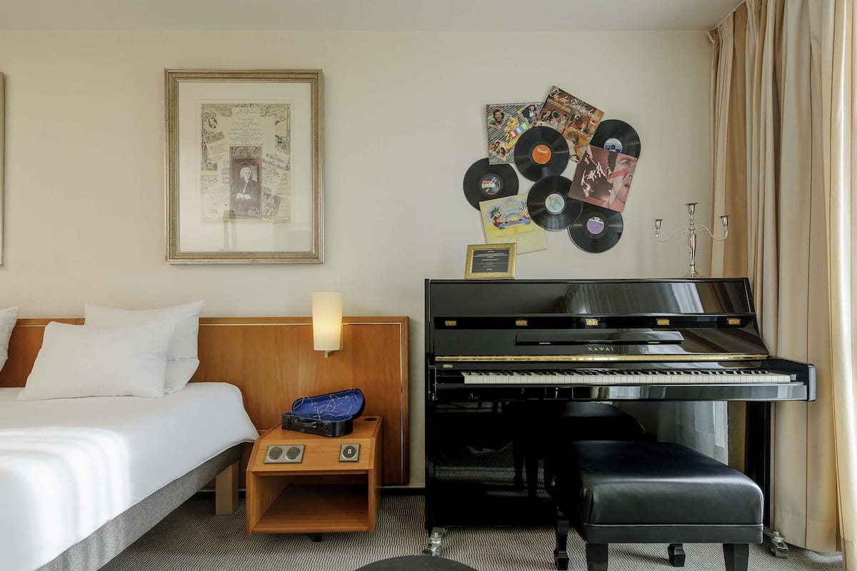 Een hotelkamer met een bed, een piano, een ingelijst kunstwerk aan de muur, en een recordcollectie bevestigd aan de muur.