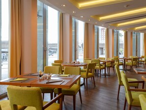 Un restaurant amb grans finestres, taules de fusta i cadires grogues.