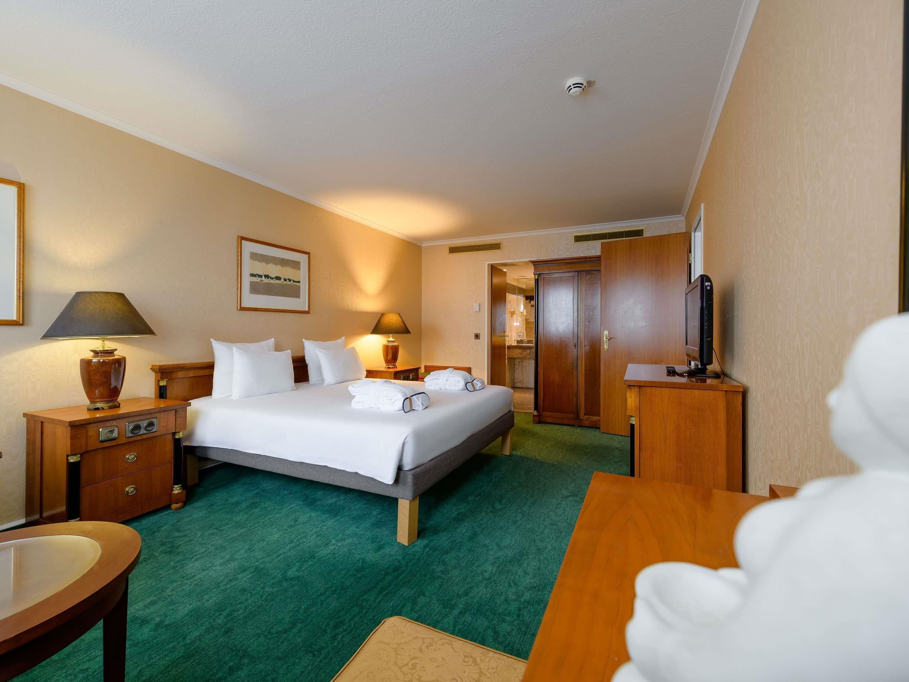 A hotel room with a bed, two bedside tables, a desk, a chair, a TV, and a door to the bathroom.