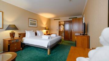 A hotel room with a bed, two bedside tables, a desk, a chair, a TV, and a door to the bathroom.