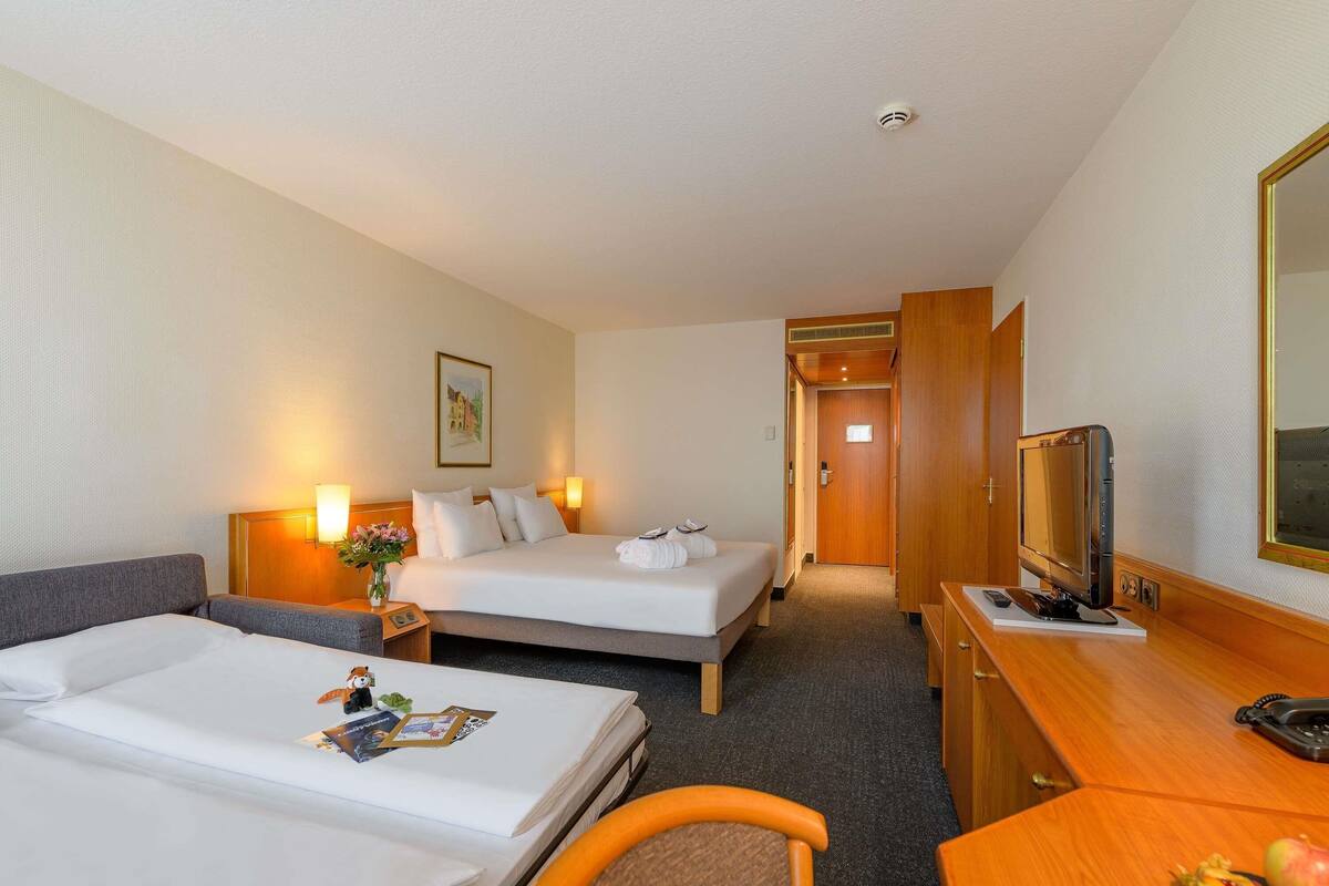 Een hotelkamer met twee bedden, een bureau met televisie en een kleine tafel met fruit.