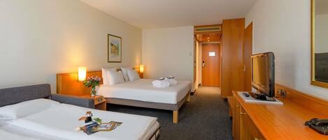 A hotel room with two beds, a desk with a television, and a small table with fruit.