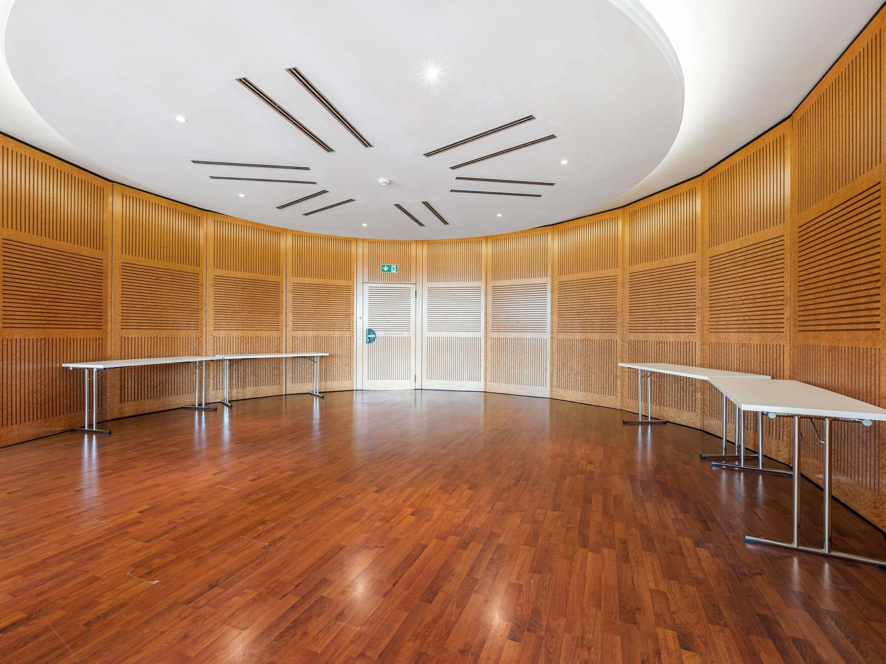 Een ruime kamer met houten paneelwanden, een gepolijste houten vloer en een plafond met een uniek ontwerp.