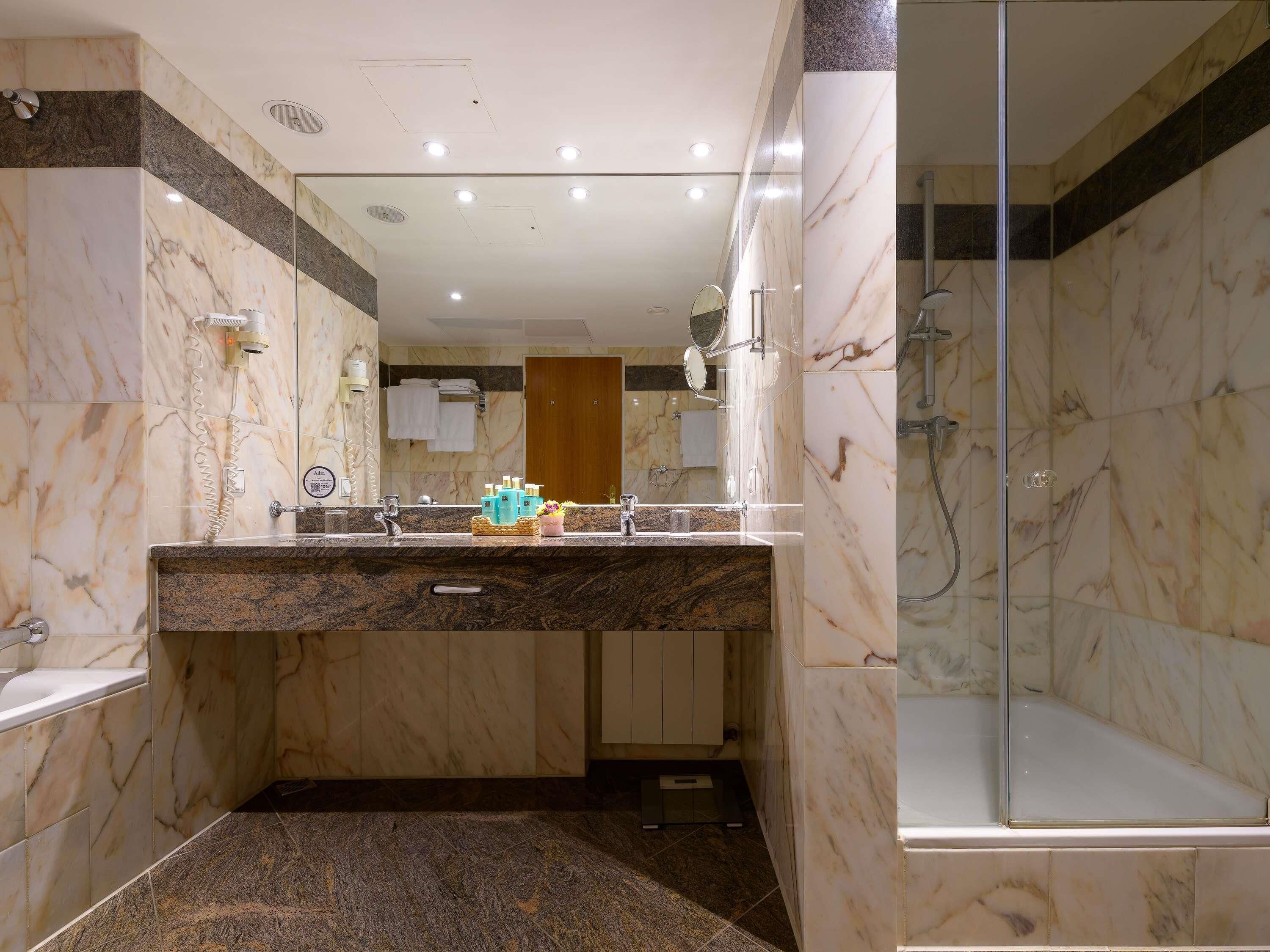 A modern bathroom with a marble vanity, a glass shower enclosure, and a wooden door.