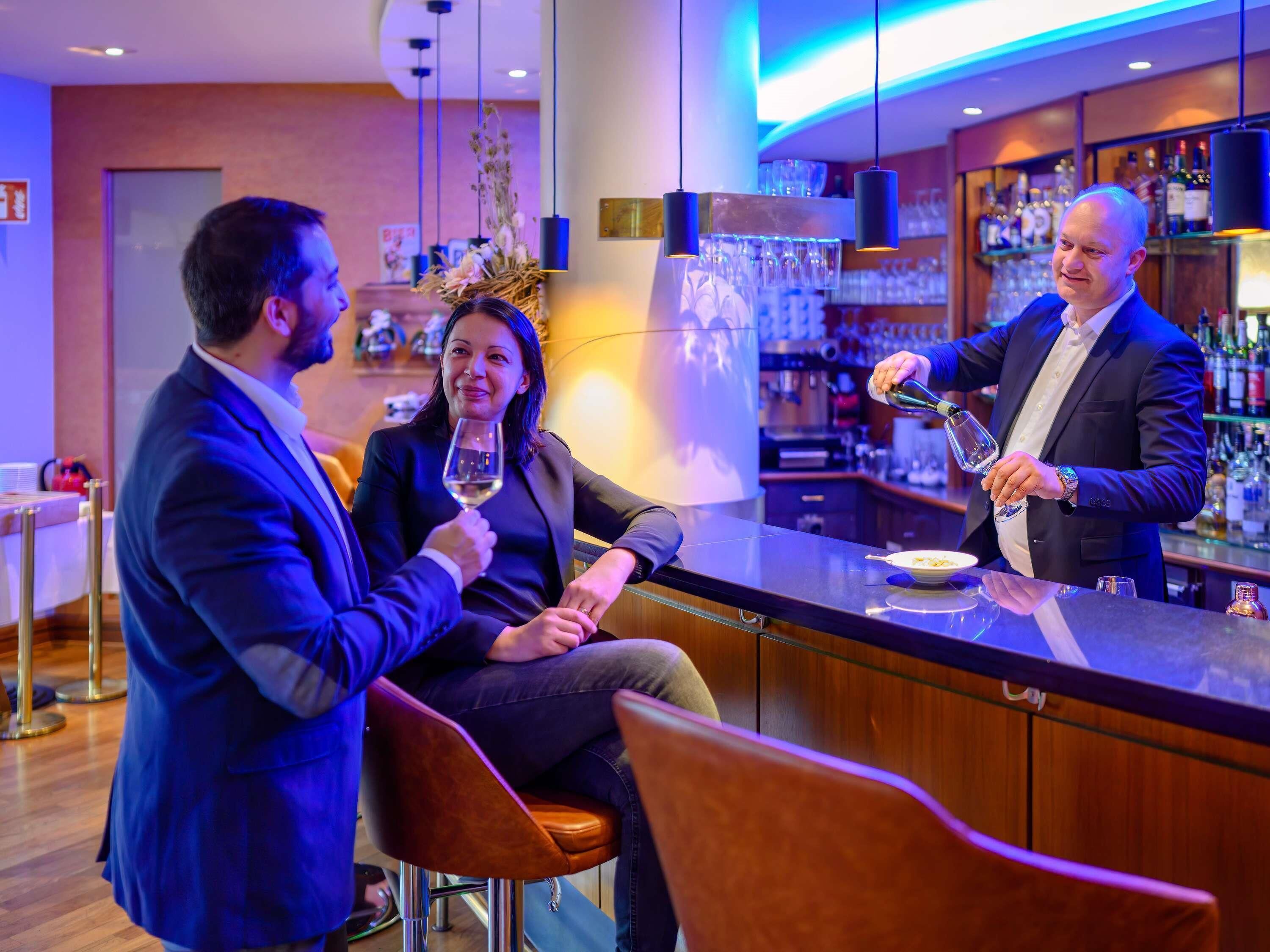 A bar area with a bartender, a seated customer, and a standing customer.