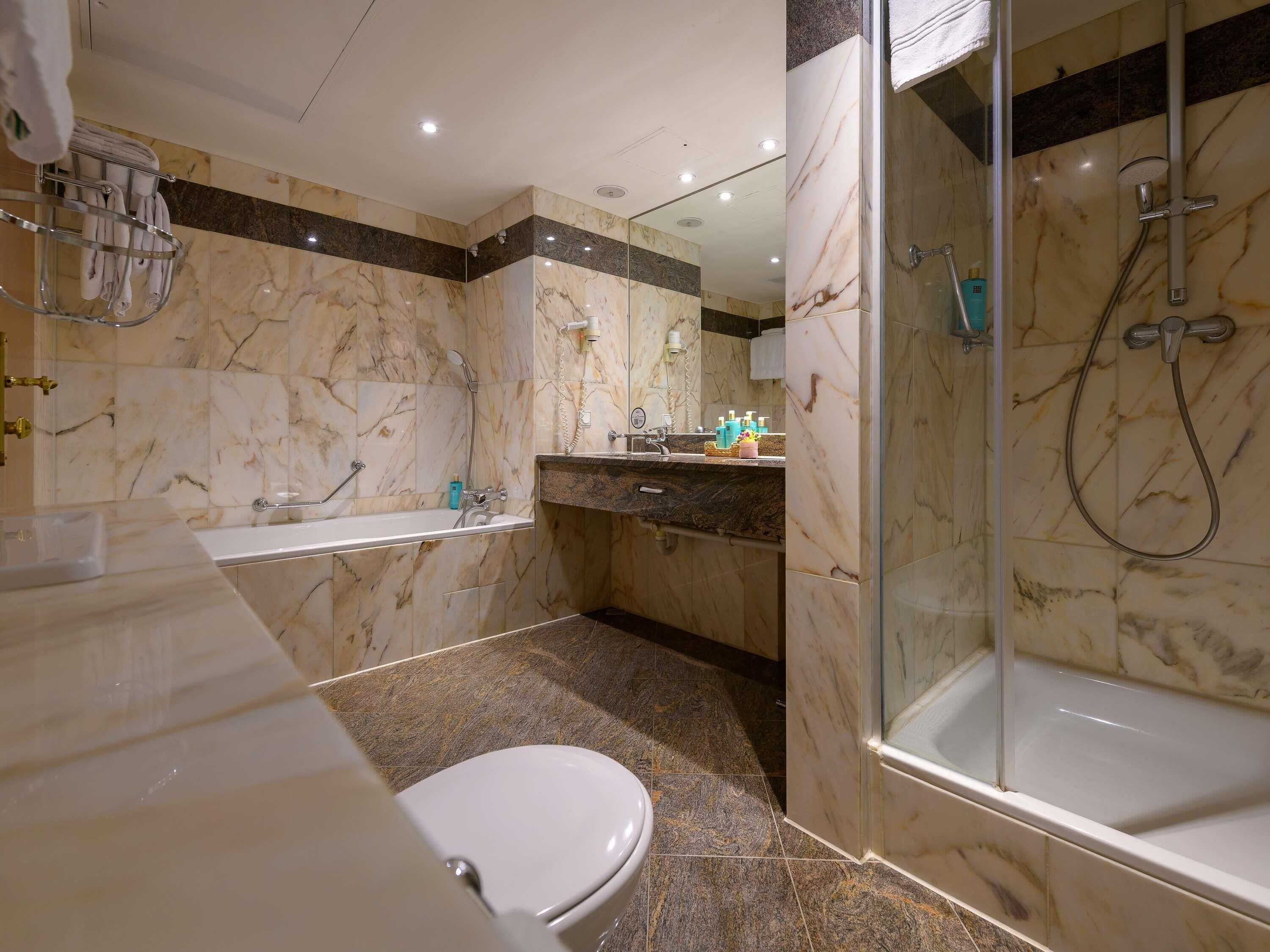 A bathroom with a bathtub, shower, toilet, and marble walls.