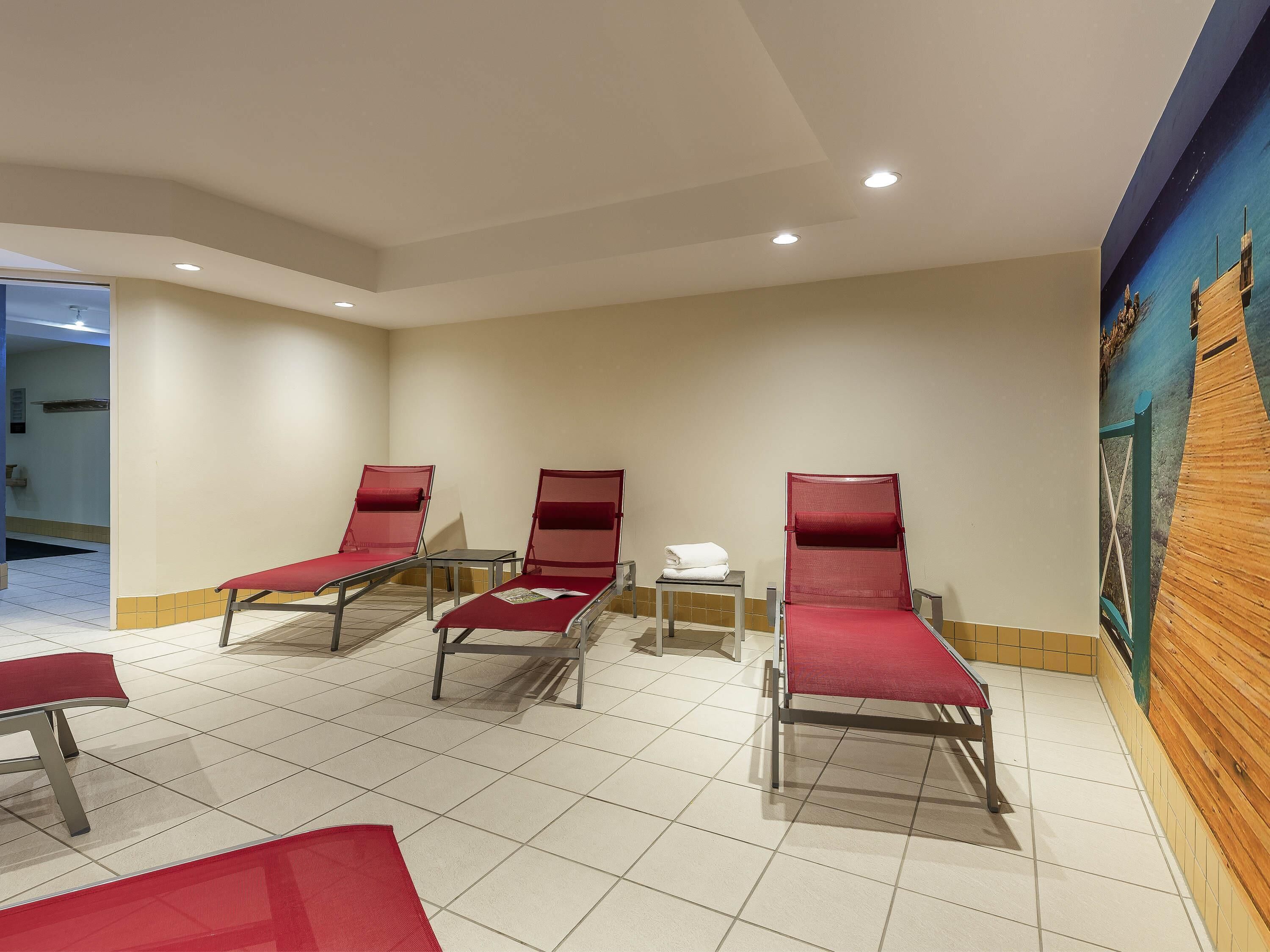 Ein Raum mit vier roten Lounge-Sesseln, einem kleinen Tisch und einem Wandbild.