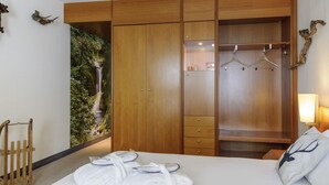 Une chambre d’hôtel avec une grande armoire en bois, un lit avec du linge de maison blanc et un porte-manteau fixé au mur.