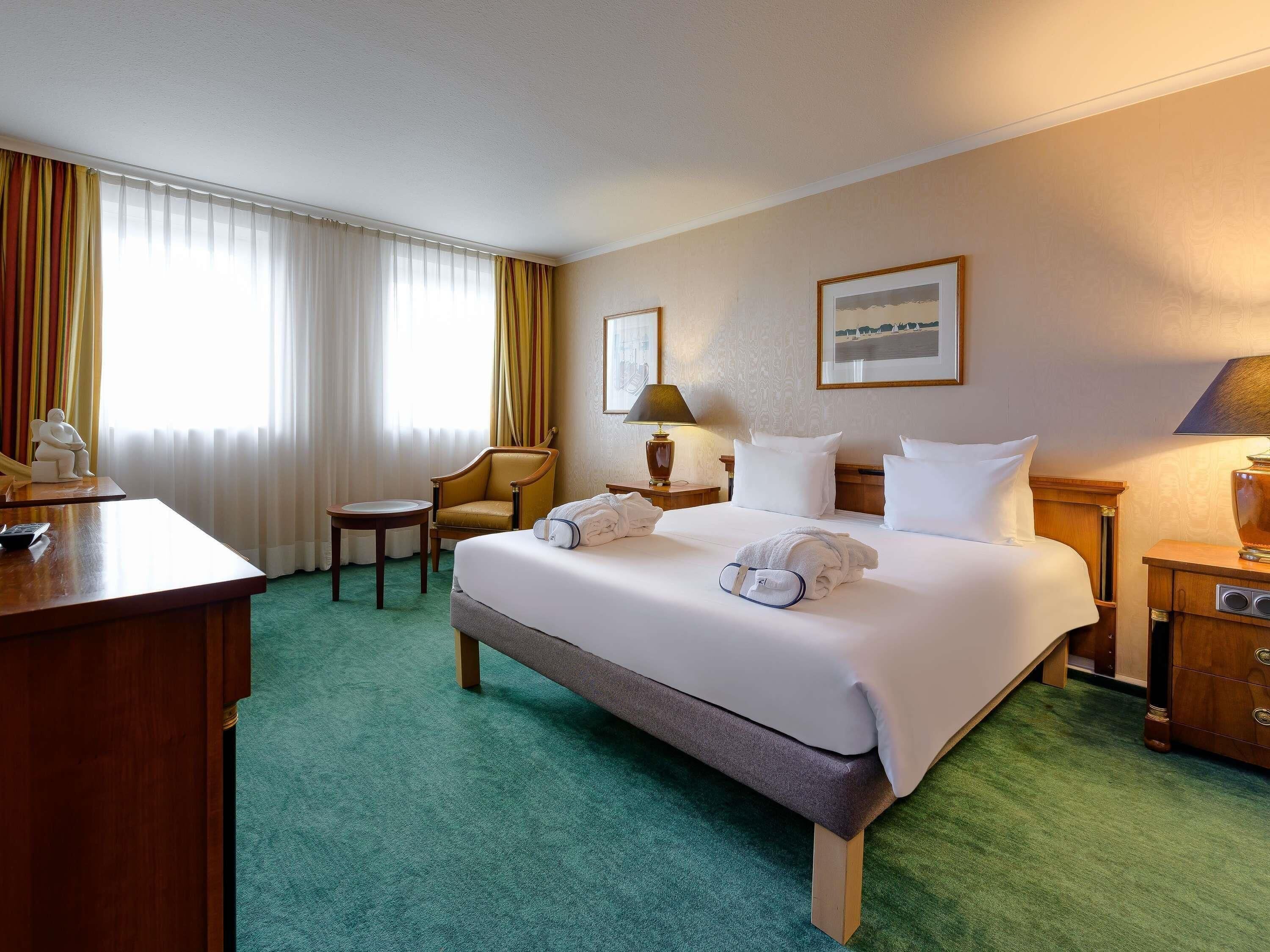 Habitació d'hotel amb un llit, una cadira, un escriptori i una làmpada.