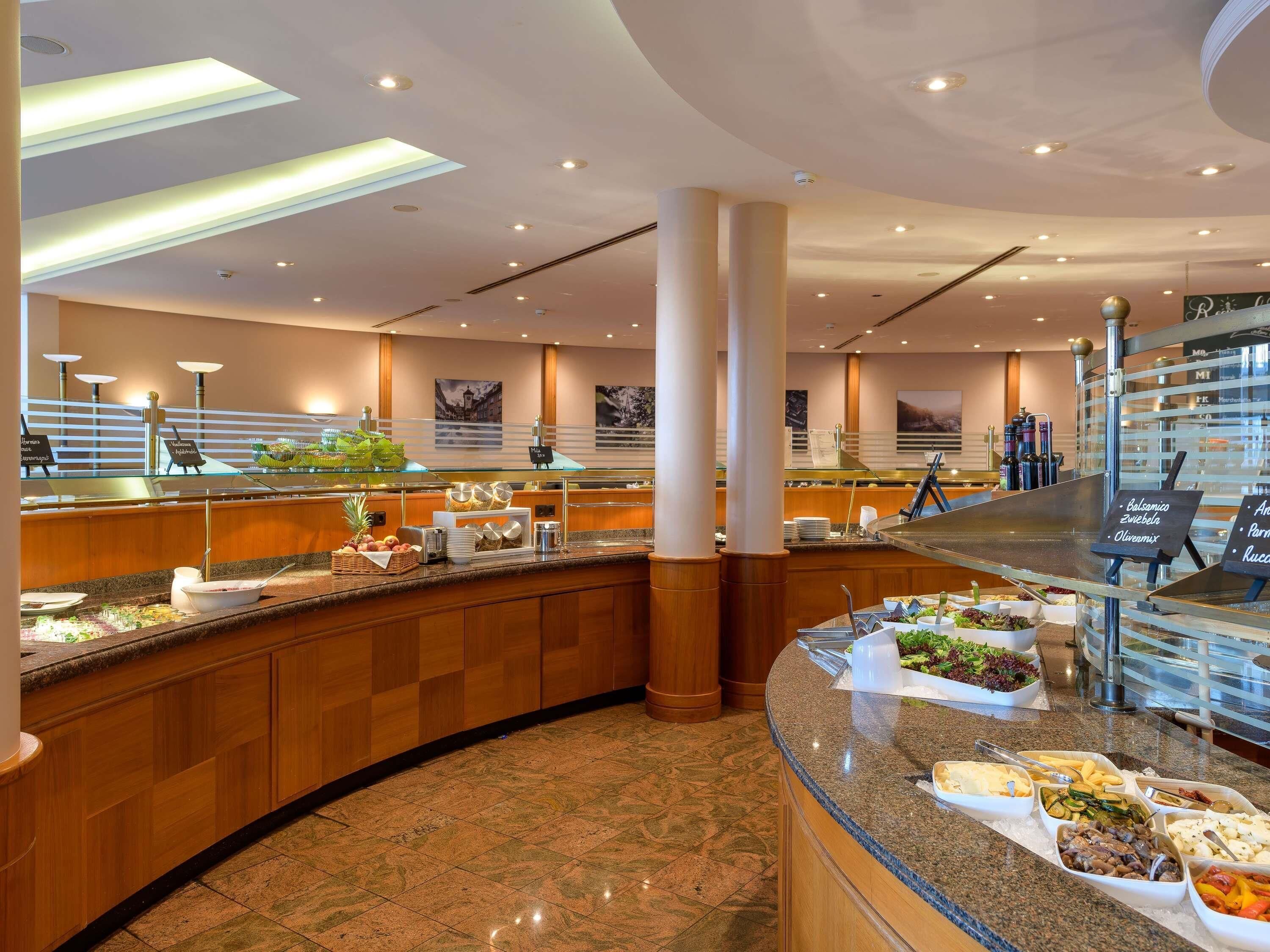 Un espace buffet proposant une grande variété de plats, notamment des salades, des fruits et des plats chauds, le tout dans un décor moderne et bénéficiant d’un éclairage abondant.